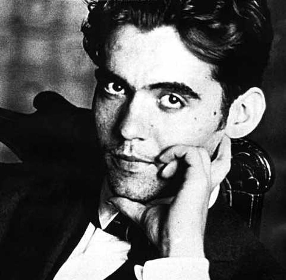 Retrato en blanco y negro de federico garcia lorca vestido con traje formal, con la barbilla apoyada en la mano y un fondo desenfocado.