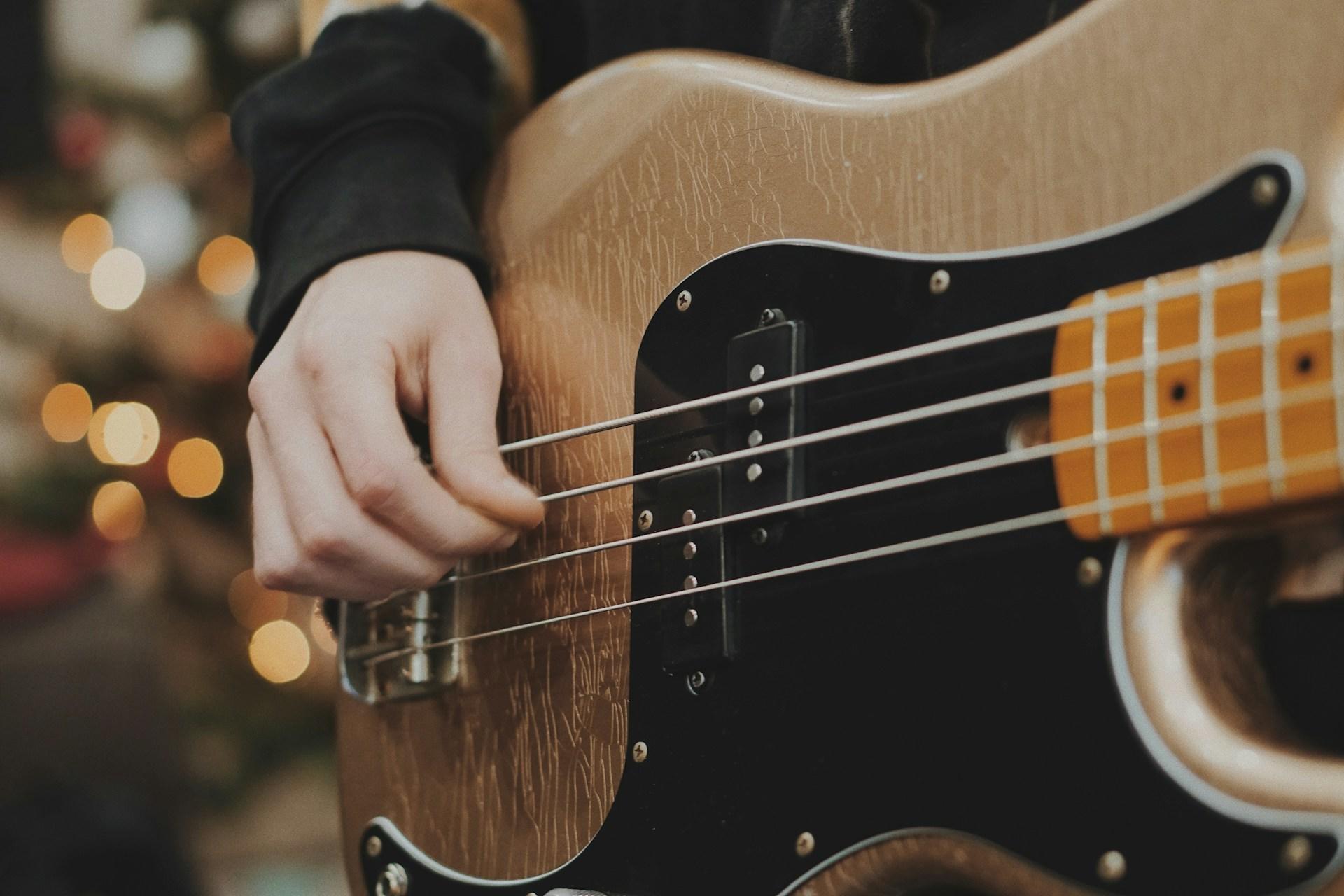 una mano derecha tocando un bajo eléctrico color café con negro.