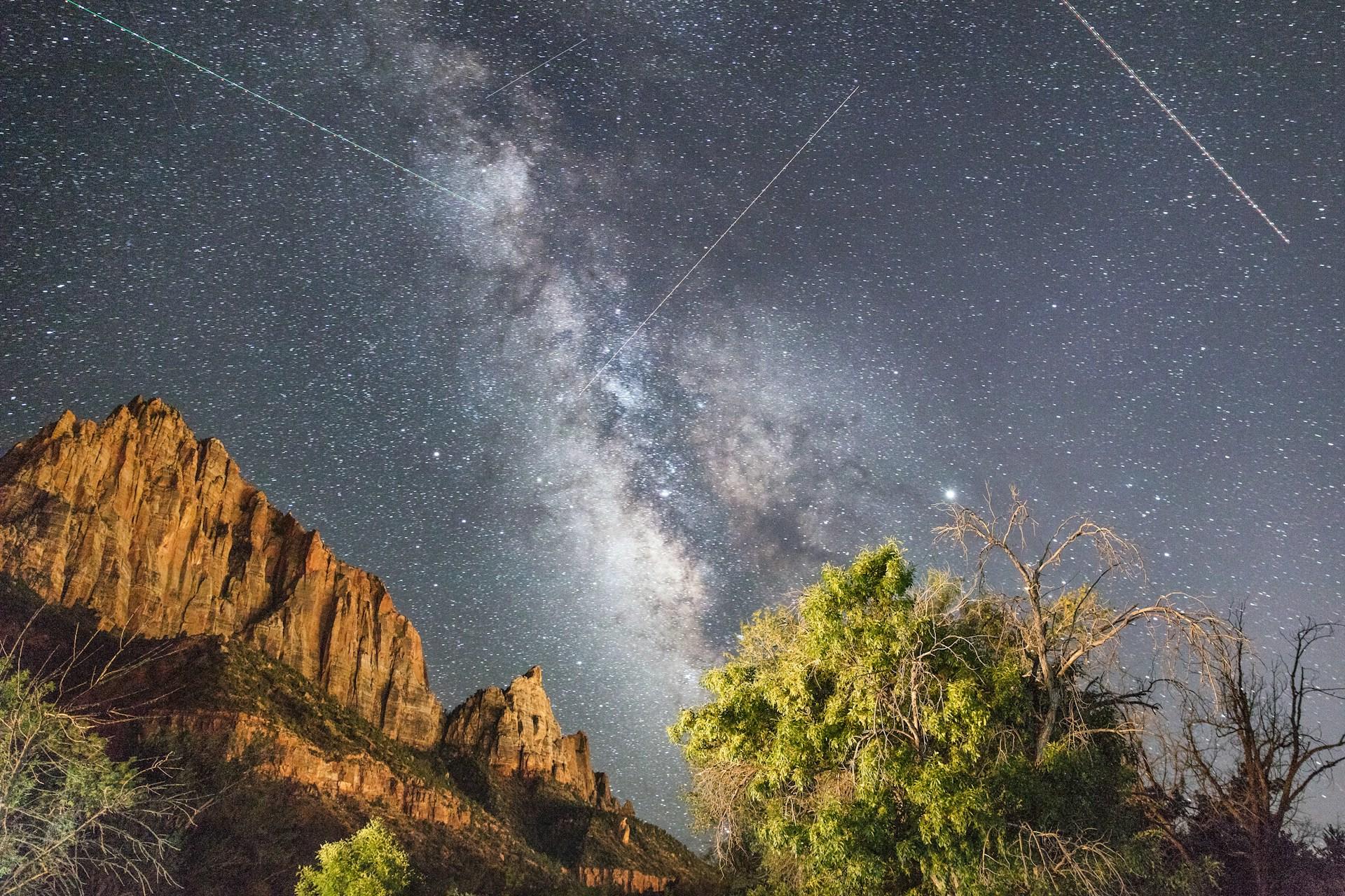 fotografia de la via lactea detrás de una montaña con árboles