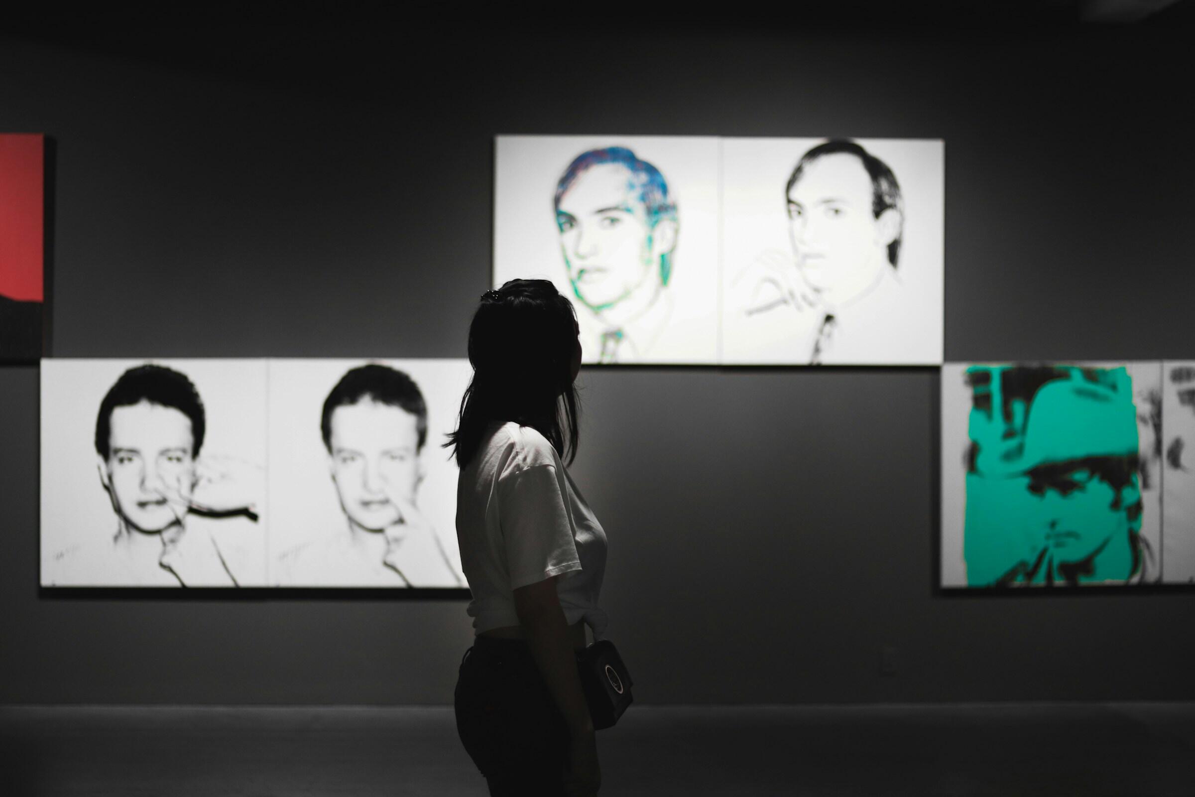 Un visitante contempla piezas de arte abstracto de andy warhol en una galería moderna, que crea una atmósfera reflexiva con colores apagados.