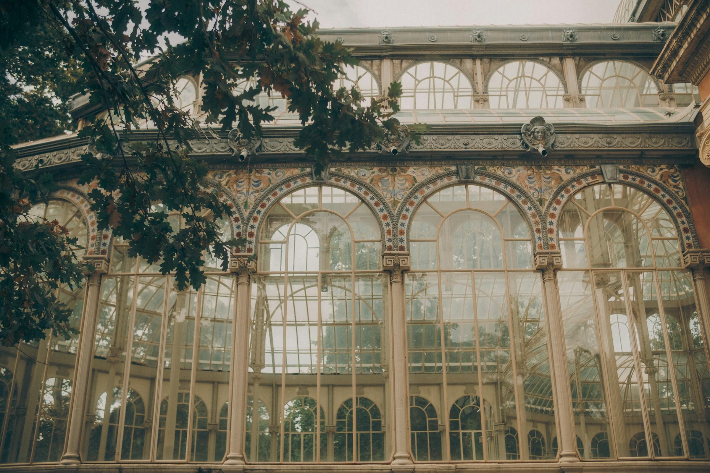 el palacio de cristal del retiro de madrid con arcos ornamentados y detalles intrincados, rodeado de exuberante vegetación bajo una luz suave y difusa.