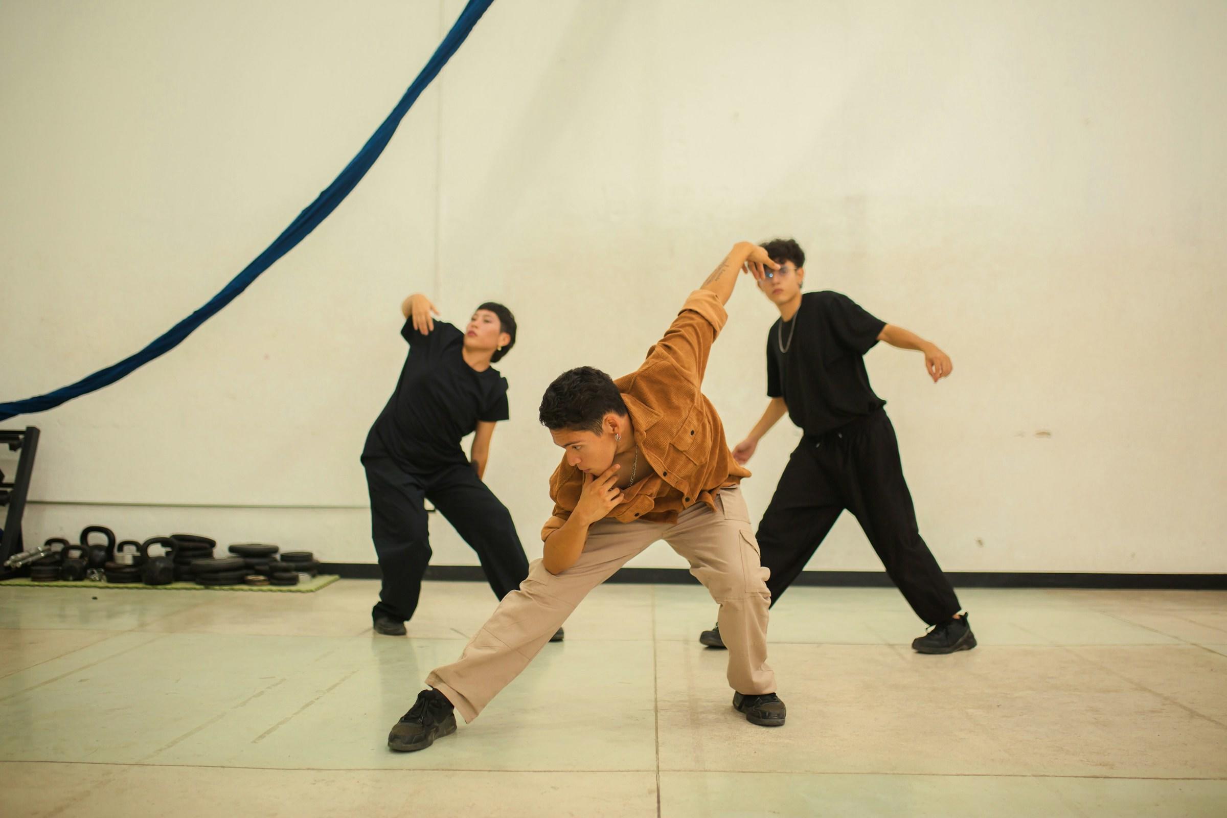 Tres personas practican movimientos de baile en un estudio.