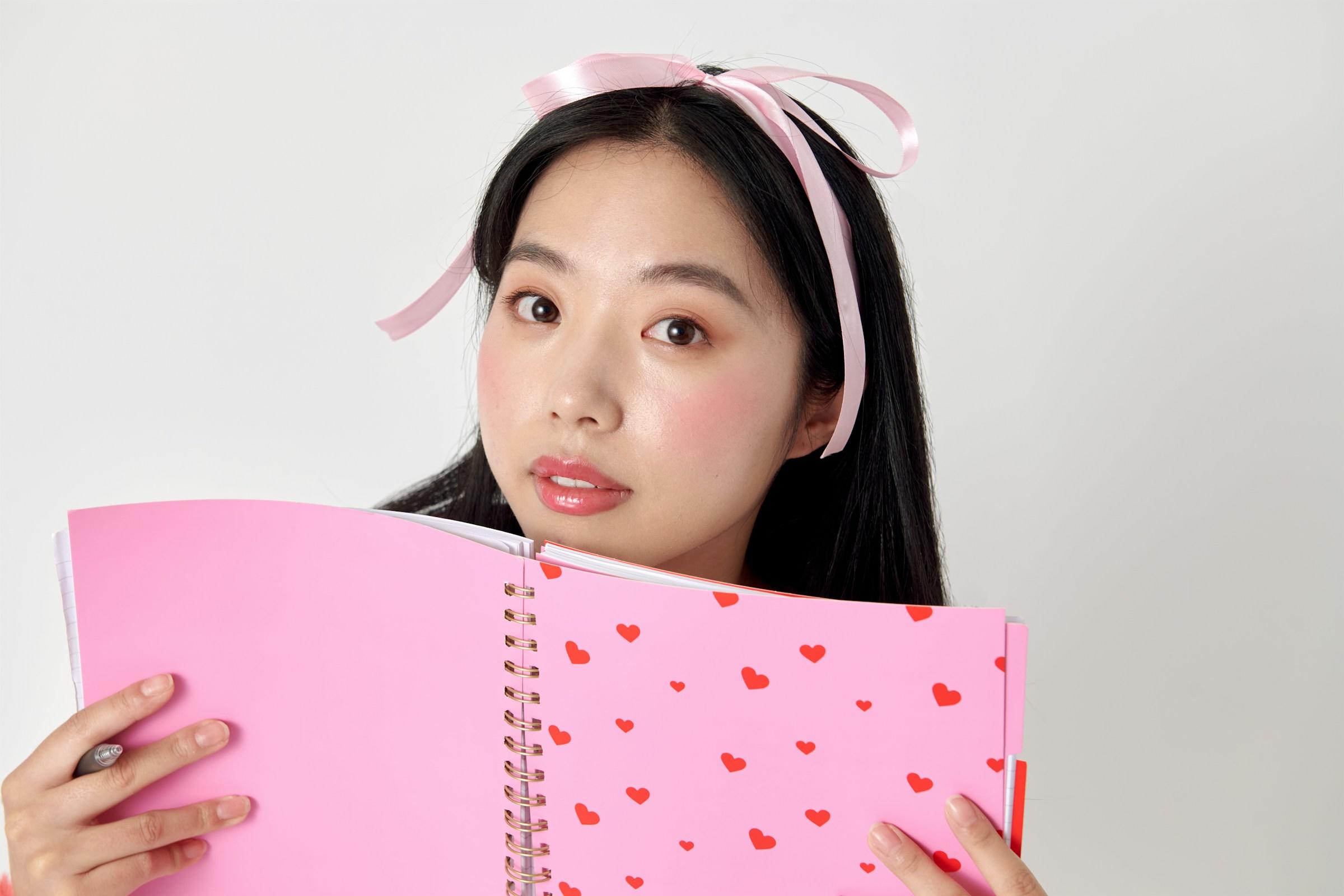 Persona sosteniendo un cuaderno rosa con corazones rojos, con un lazo en el pelo.