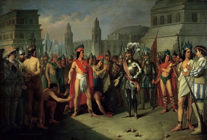 Una pintura histórica que representa un encuentro entre un conquistador europeo con armadura y unos líderes indígenas con trajes tradicionales, con una arquitectura antigua como telón de fondo.