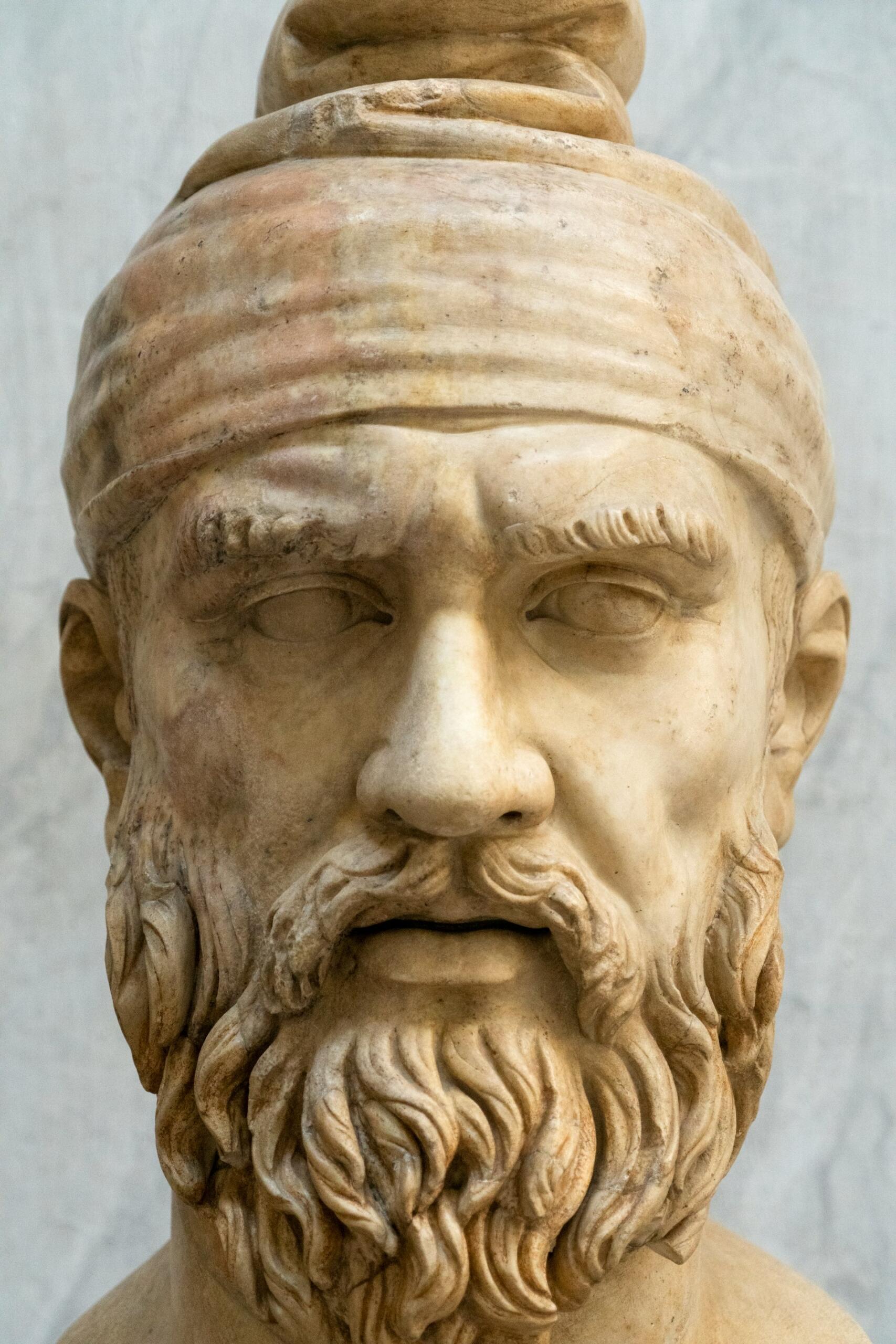 Primer plano de una escultura clásica de Heródoto que muestra texturas detalladas del cabello y la barba, con un fondo liso que realza sus rasgos.