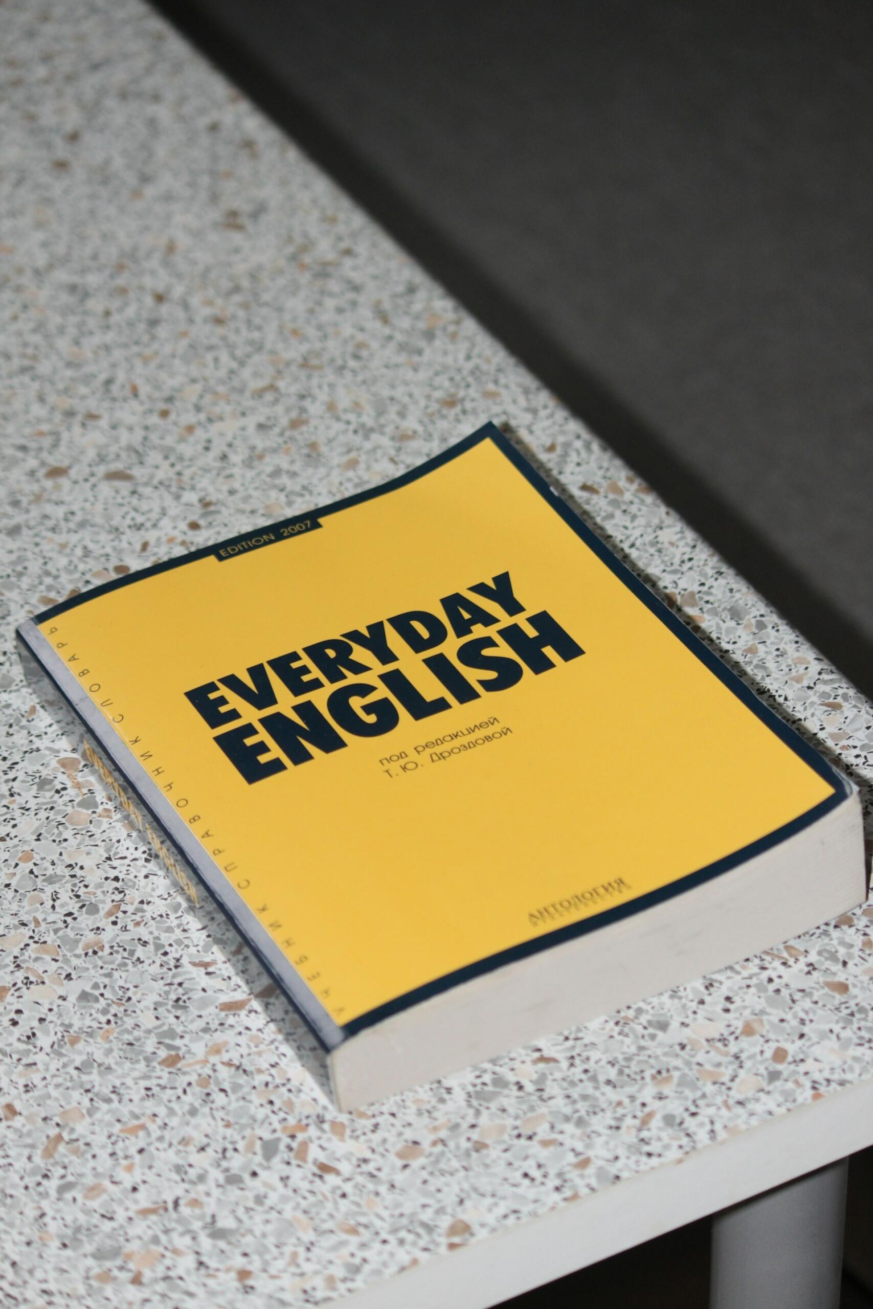 Un libro amarillo de aprendizaje de inglés titulado «Everyday English» sobre una encimera moteada, que transmite un ambiente práctico y centrado en el estudio.