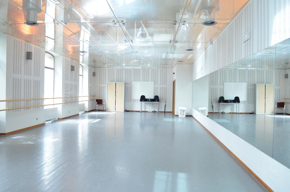 Estudio de danza luminoso y espacioso con espejos, barra de ballet de madera y grandes ventanas, con luz que se refleja en el suelo brillante.