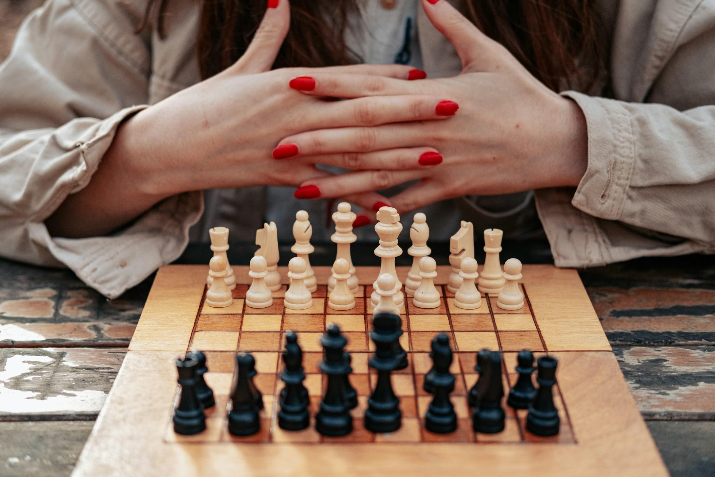 Persona con las uñas rojas contemplando una partida de ajedrez en curso