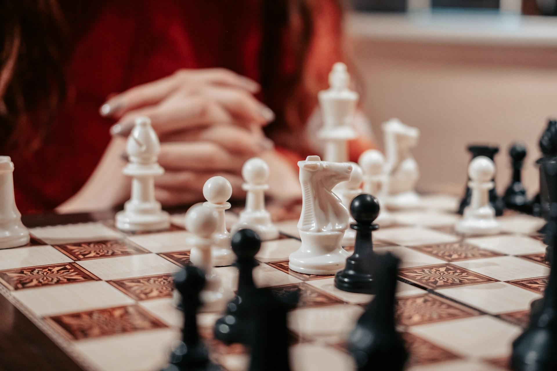 Una persona contempla concentrada las jugadas de ajedrez, con las manos juntas cerca de un tablero.
