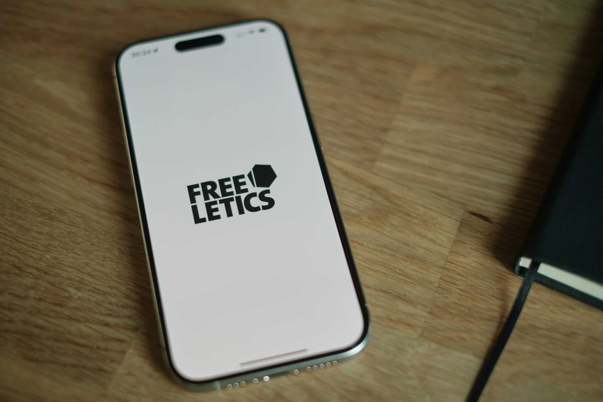 Smartphone con el logotipo de «Freeletics» en la pantalla, sobre una superficie de madera junto a un cuaderno negro.