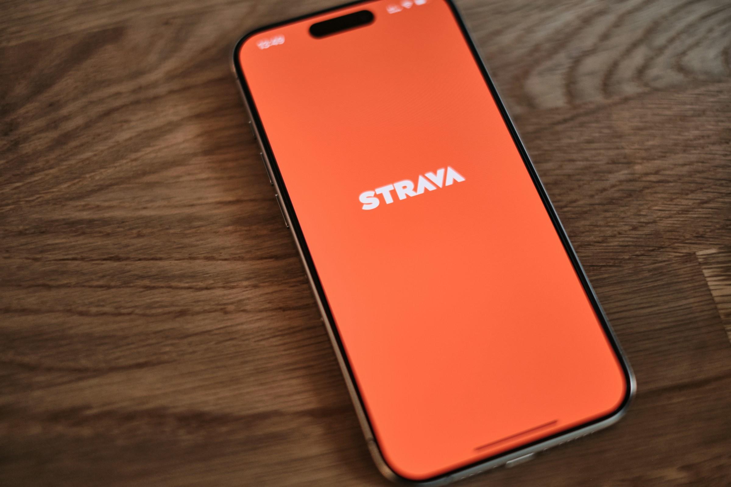 Smartphone con el logotipo de la aplicación Strava en la pantalla tumbado sobre una superficie de madera.