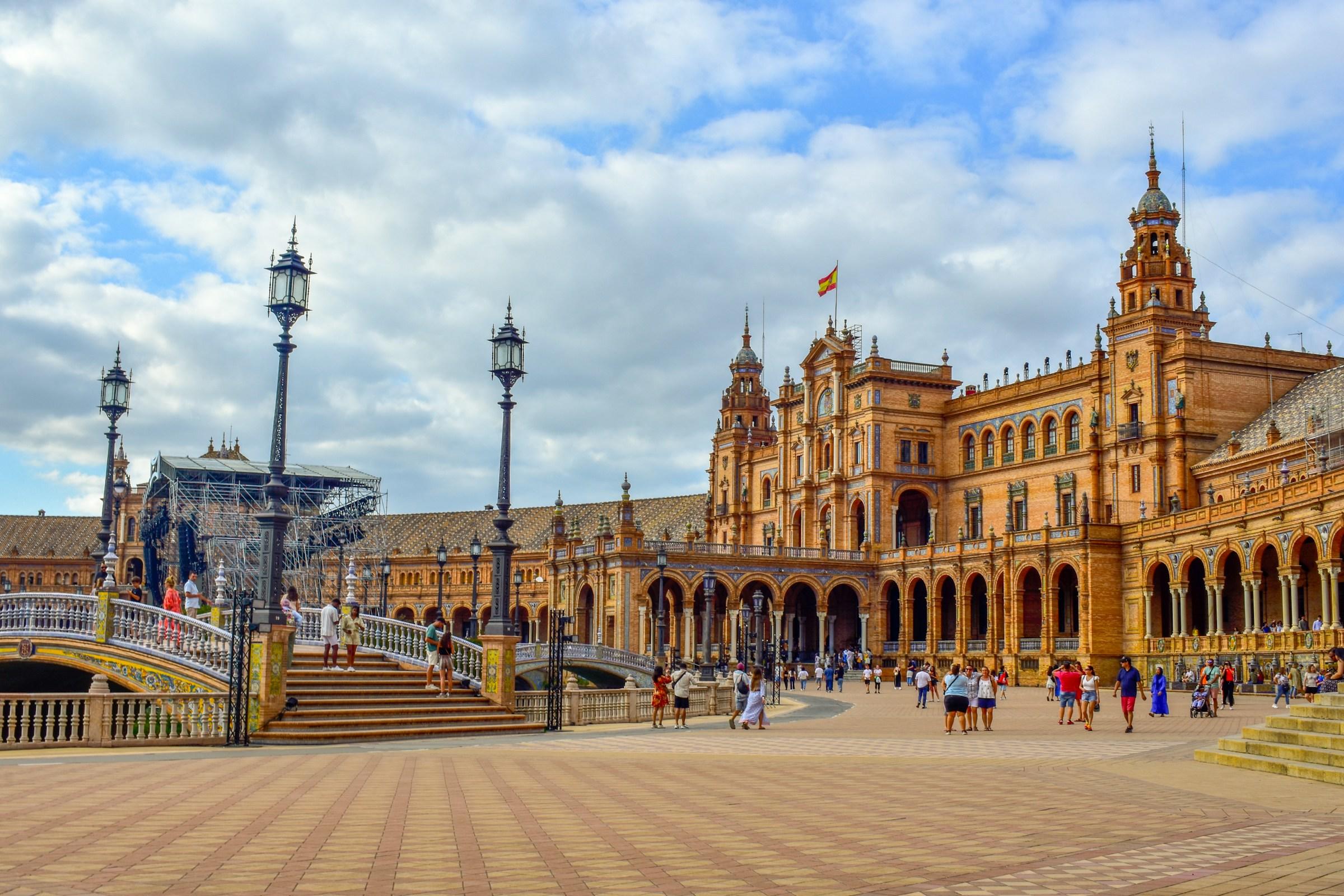 Plaza de España de Sevilla: arquitectura ornamental, puente y visitantes bajo un cielo nublado.