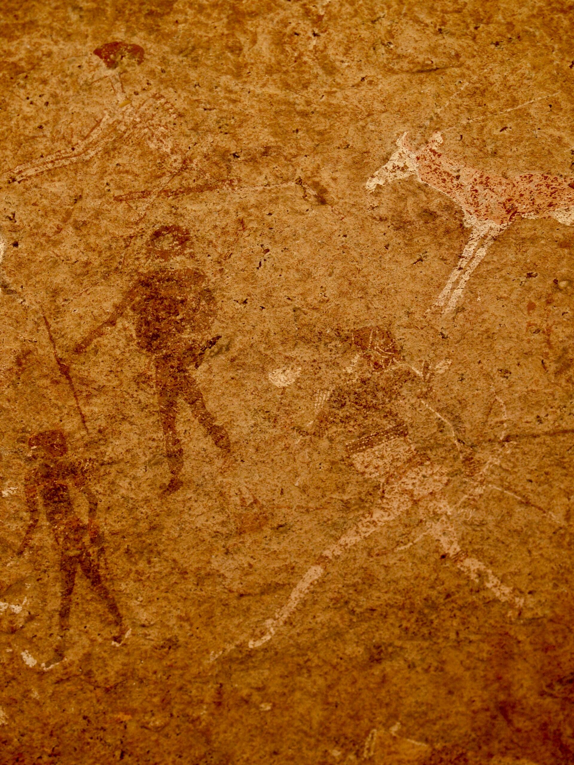 Arte rupestre antiguo que representa figuras humanas con lanzas, posiblemente cazadores, y animales sobre un fondo terroso y texturizado. Transmite una sensación de historia y supervivencia.