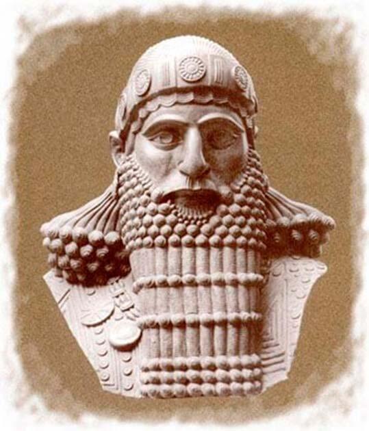 Una escultura de piedra muy detallada que representa a un guerrero de la antigüedad con una barba ornamentada, casco y armadura. La imagen transmite fuerza e historia.