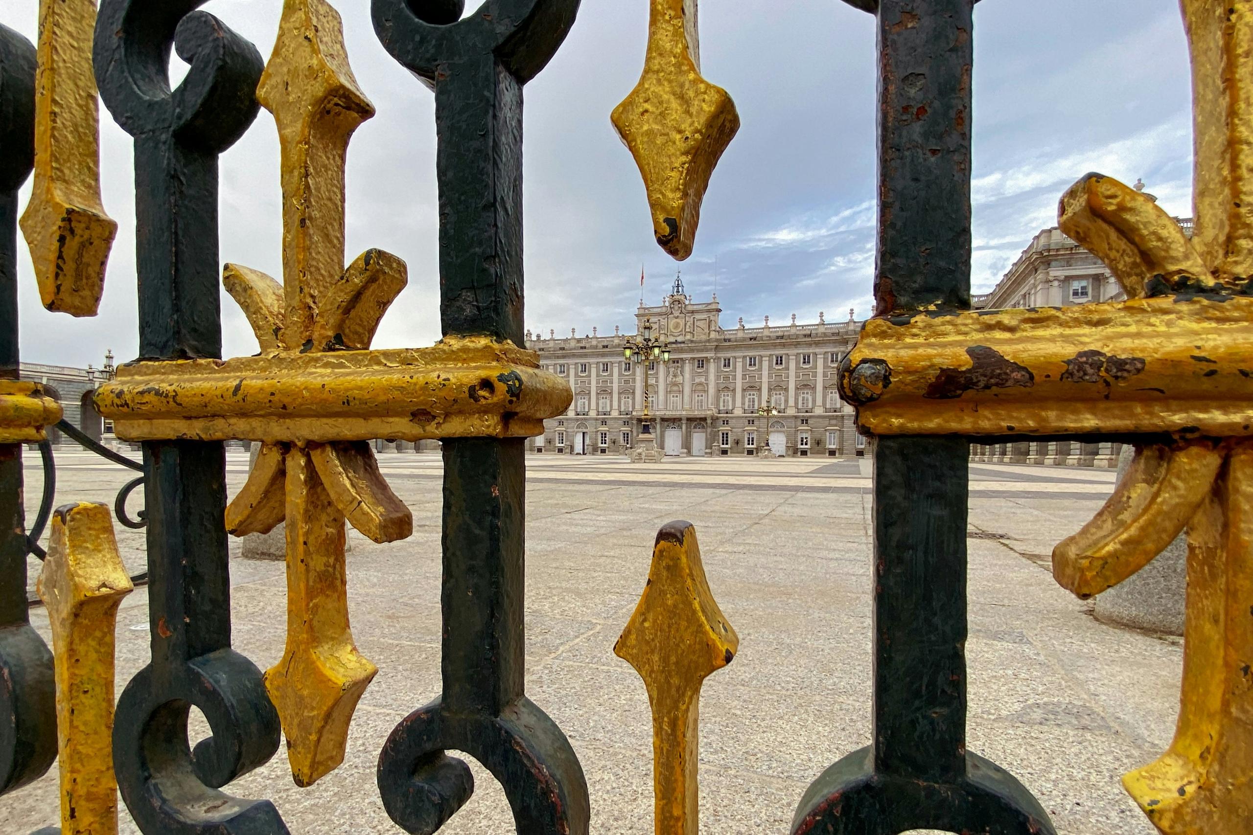 Puerta ornamentada en negro y oro con una vista del Palacio Real de Madrid al fondo.