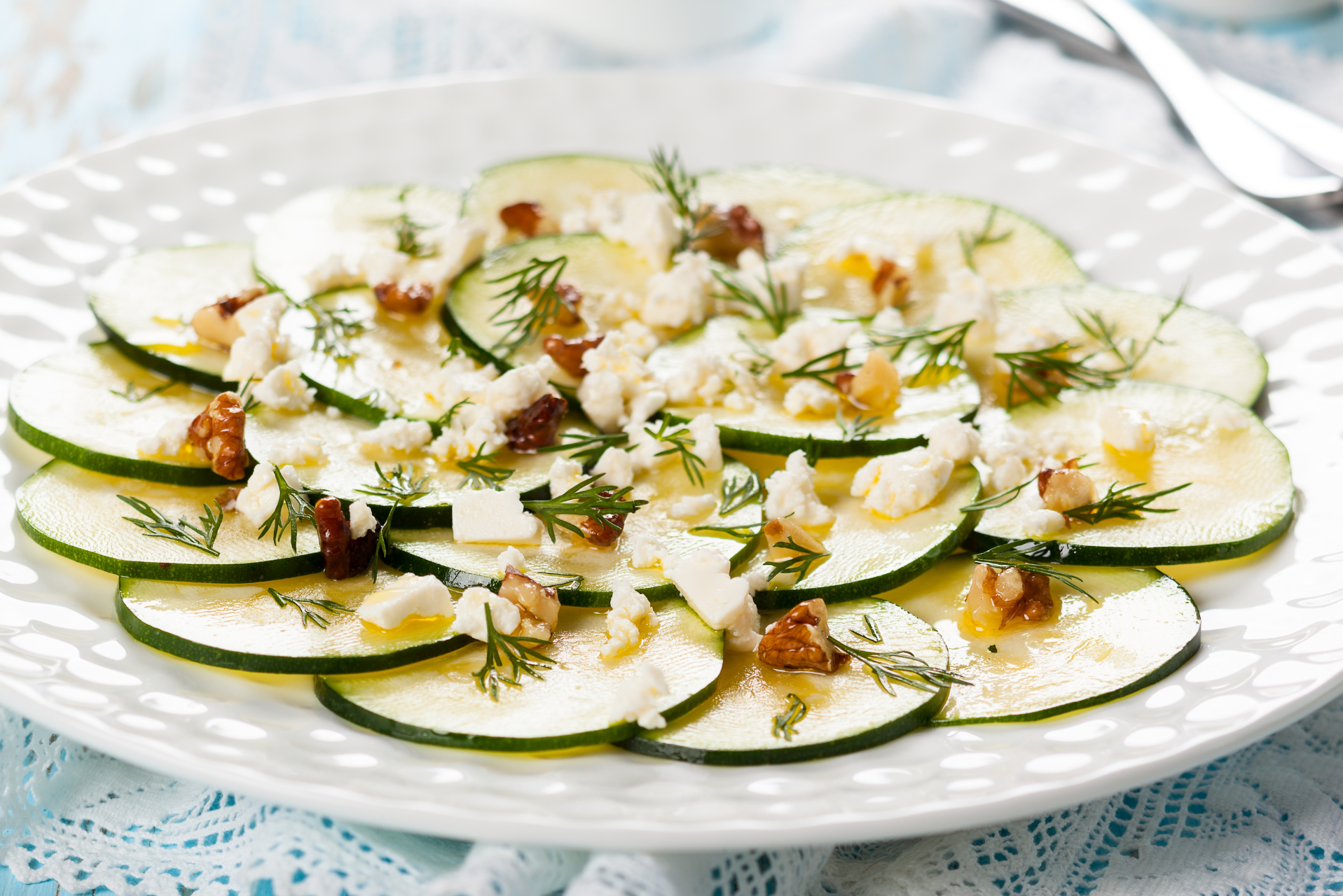 Carpaccio de calabacín con queso feta, nueces y eneldo en un plato blanco.