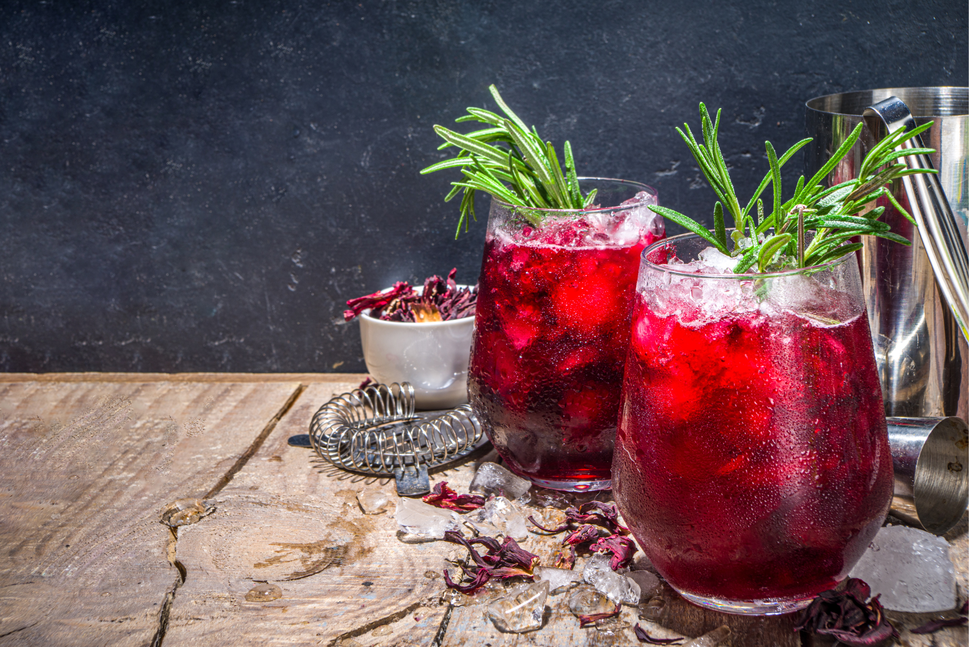 Dos copas de bebida de hibiscus decoradas con ramitas de romero, listas para disfrutar en una mesa elegante.