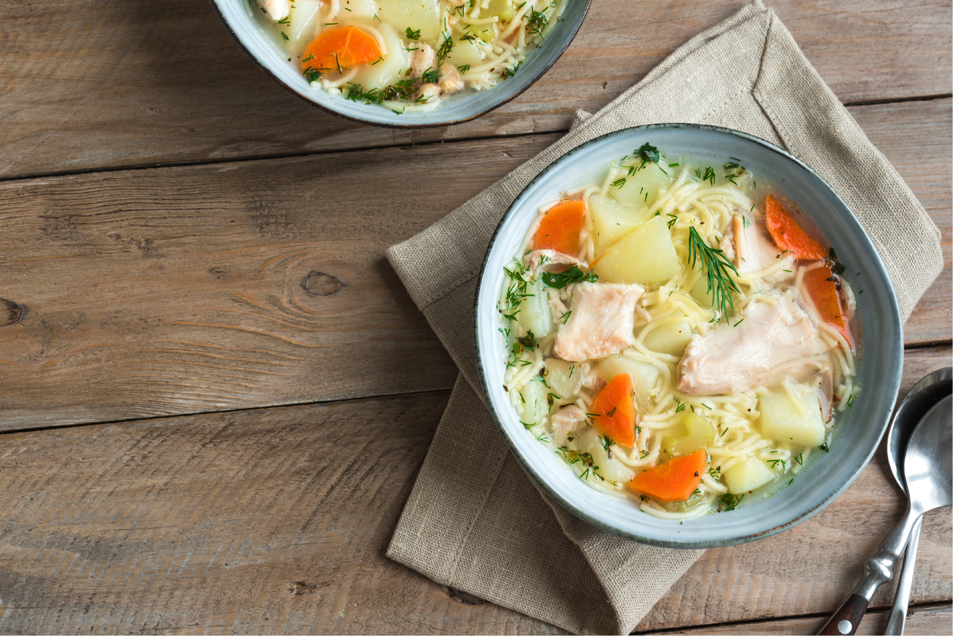 plato de sopa de pollo con papas, zanahoria y romero sobre una mesa de madera.