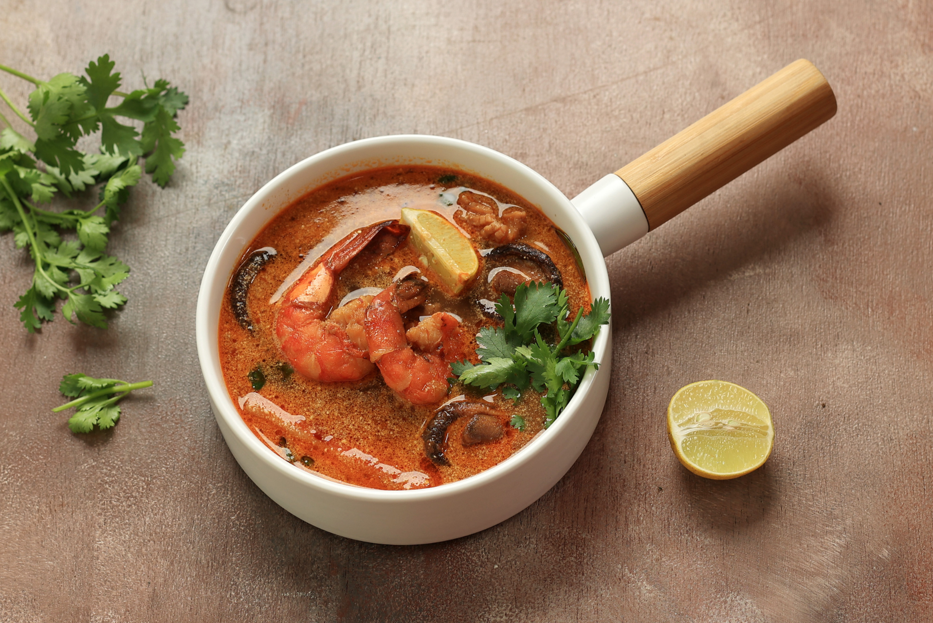 Tazón de sopa de marisco con gambas, limón y cilantro sobre una mesa de madera.