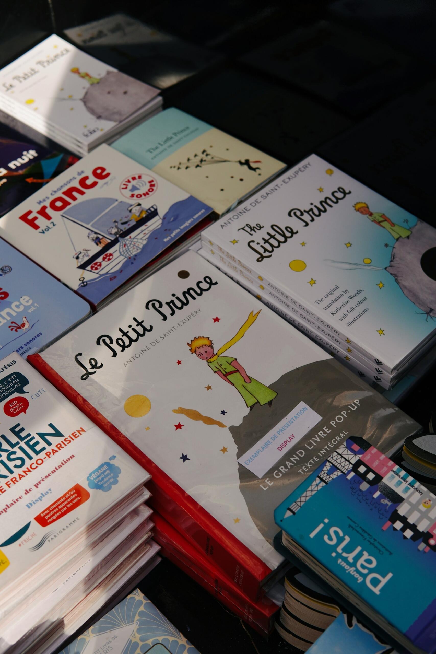 Se exponen diversas ediciones de «El principito» junto con otros libros de temática francesa. Las portadas muestran al emblemático personaje y cuentan con ilustraciones llenas de colorido.