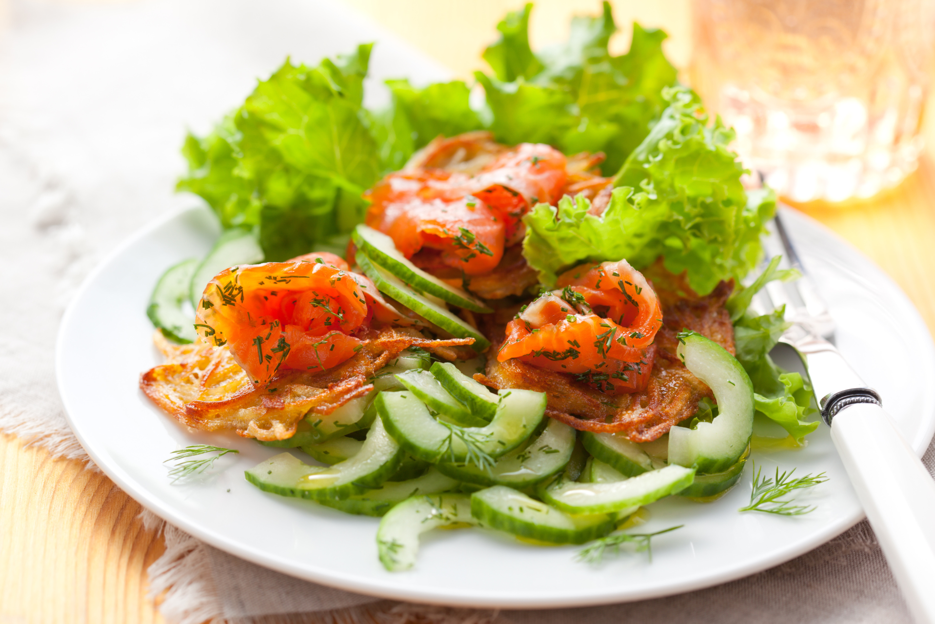 Un plato con salmón ahumado, eneldo fresco, rodajas de pepino y lechuga.
