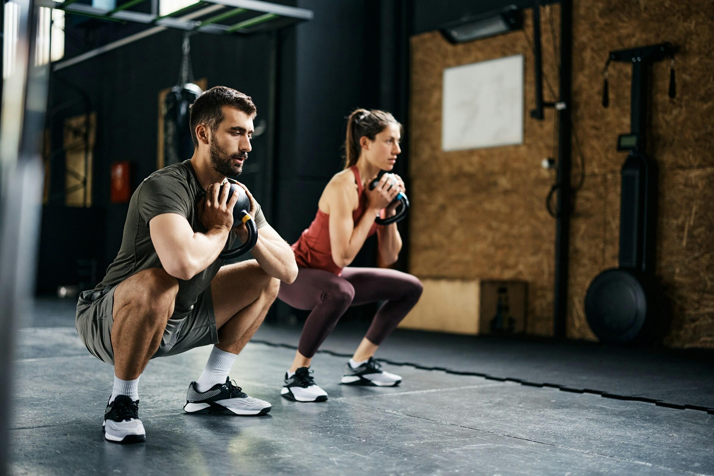 Dos personas realizan sentadillas con peso en un gimnasio.