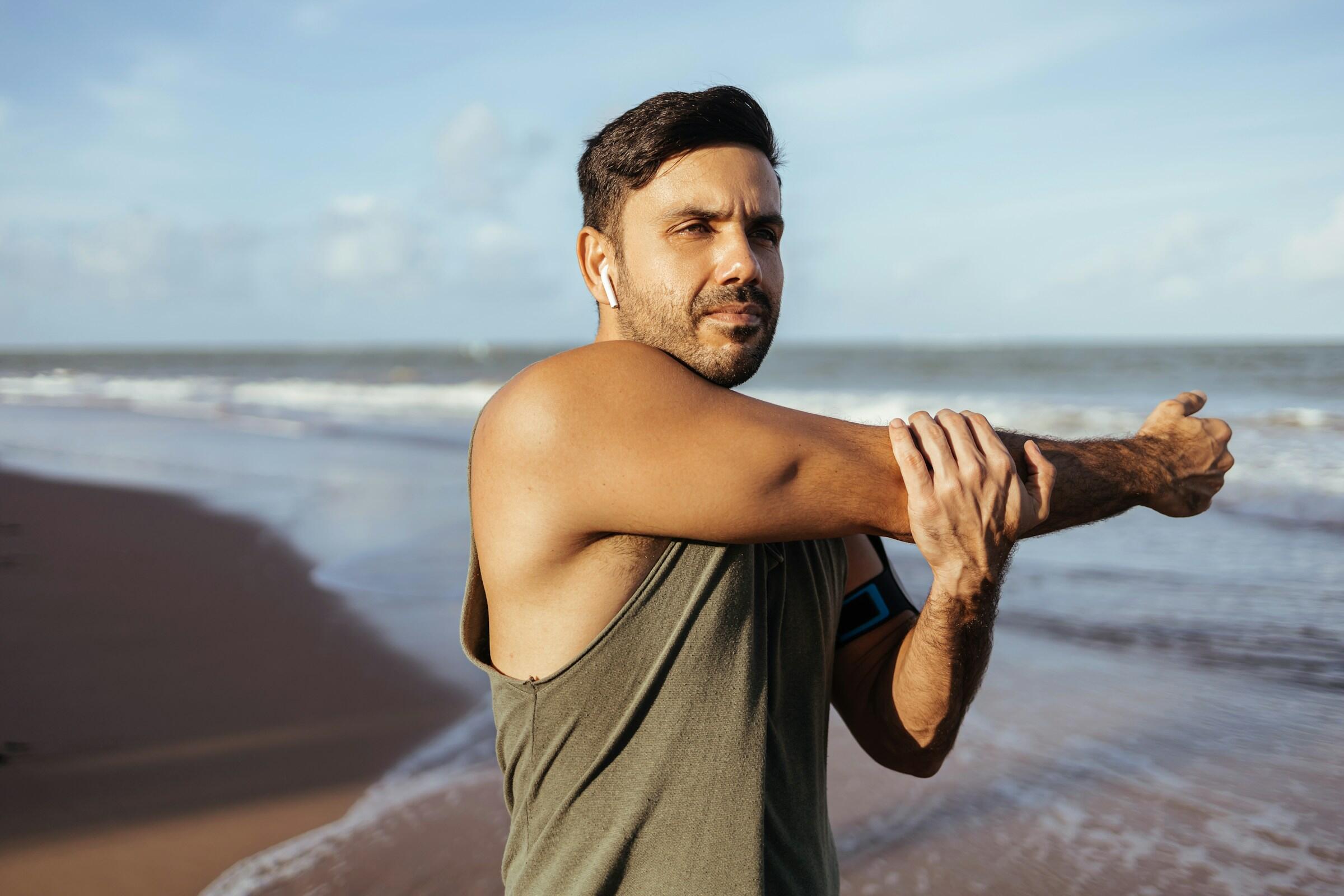 Persona estirando el brazo junto a la playa con olas de fondo.
