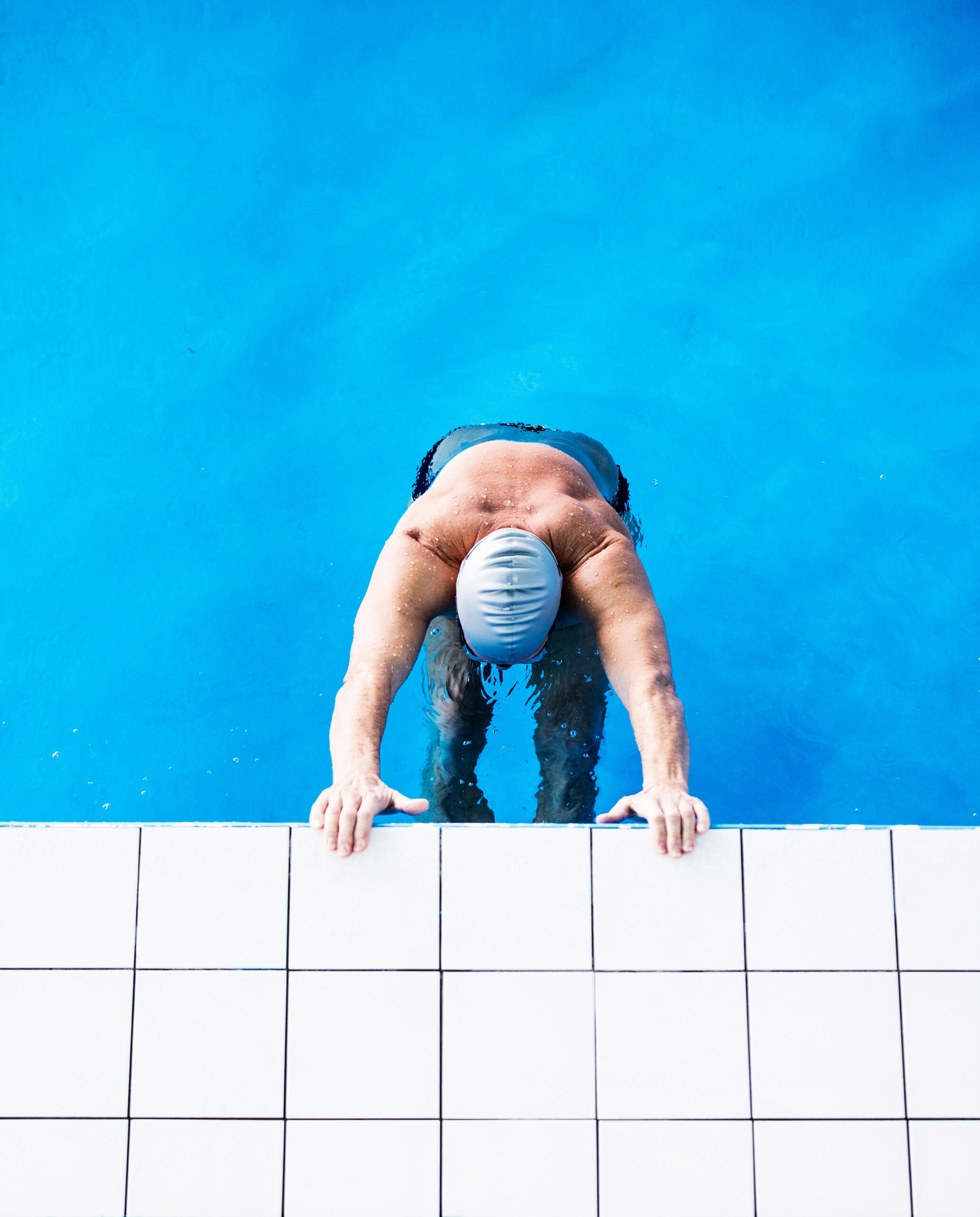 Persona con gorro de natación agarrada al borde de la piscina bajo el agua.