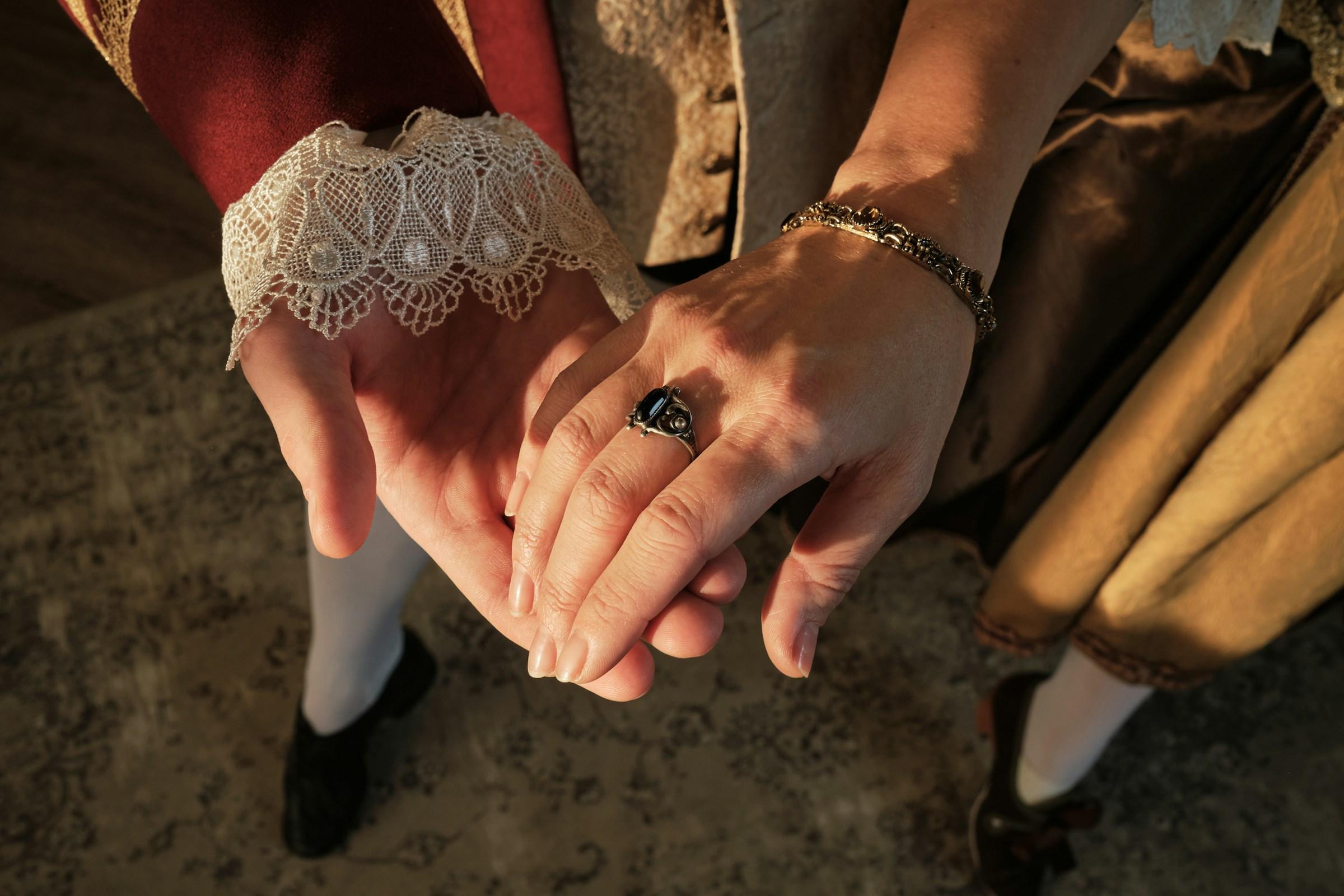 Dos manos entrelazadas, una con un puño de encaje y la otra con un anillo.