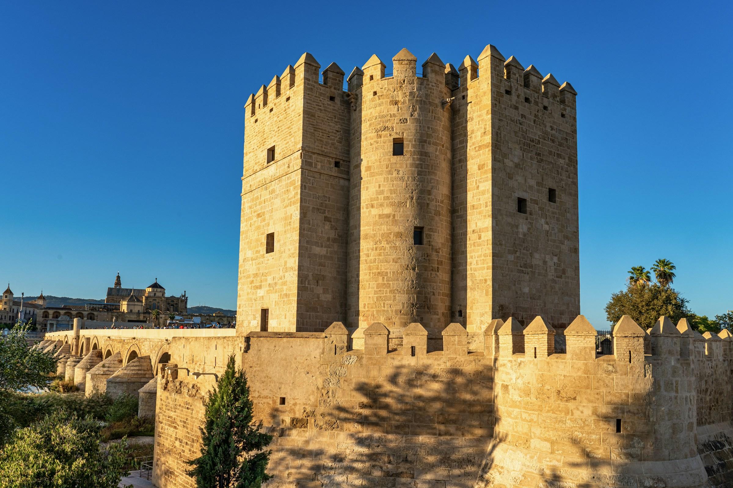 Torre medieval de piedra y muralla fortificada bajo un cielo azul despejado.
