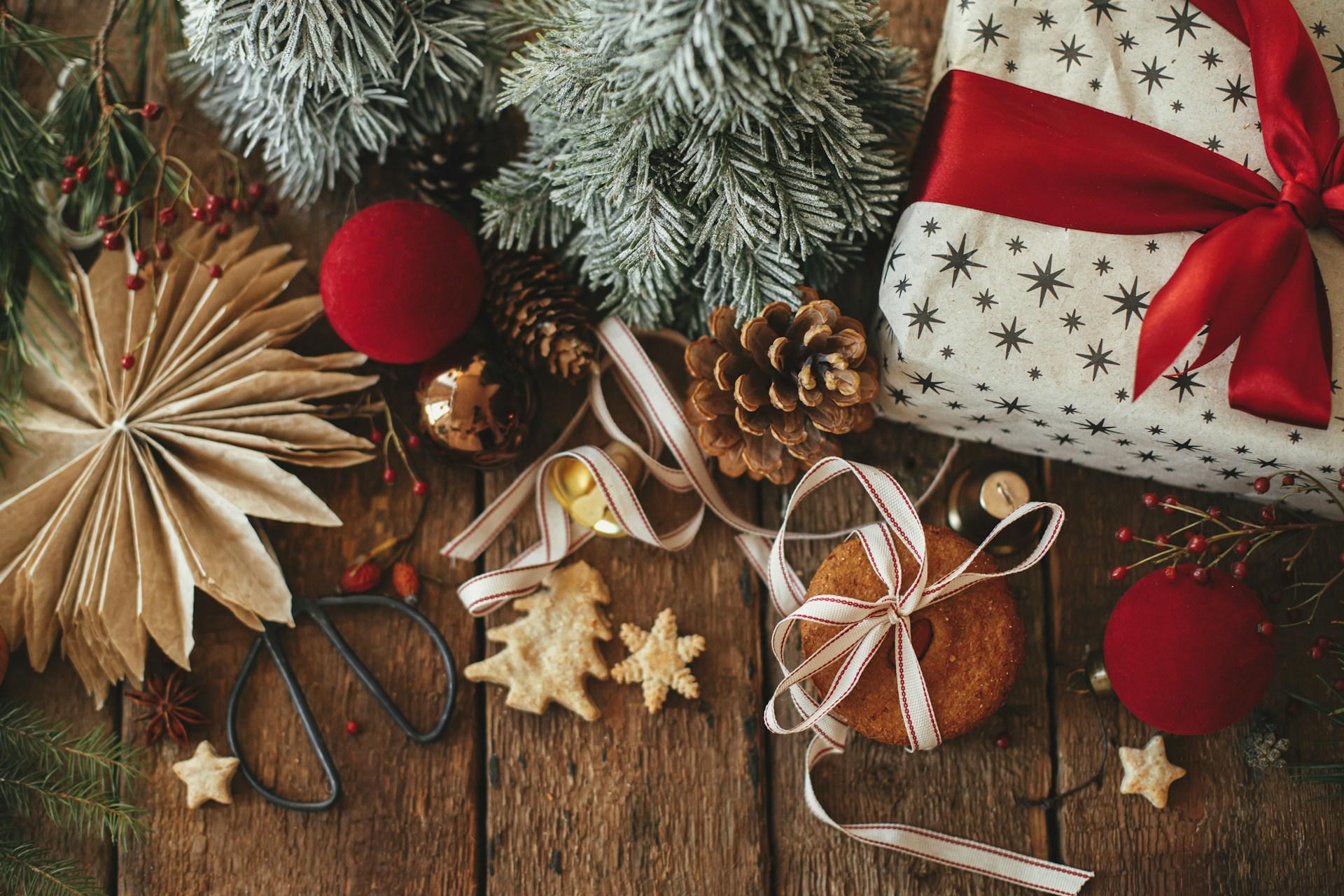 Decoración navideña con regalo envuelto, piñas y galletas sobre superficie de madera.