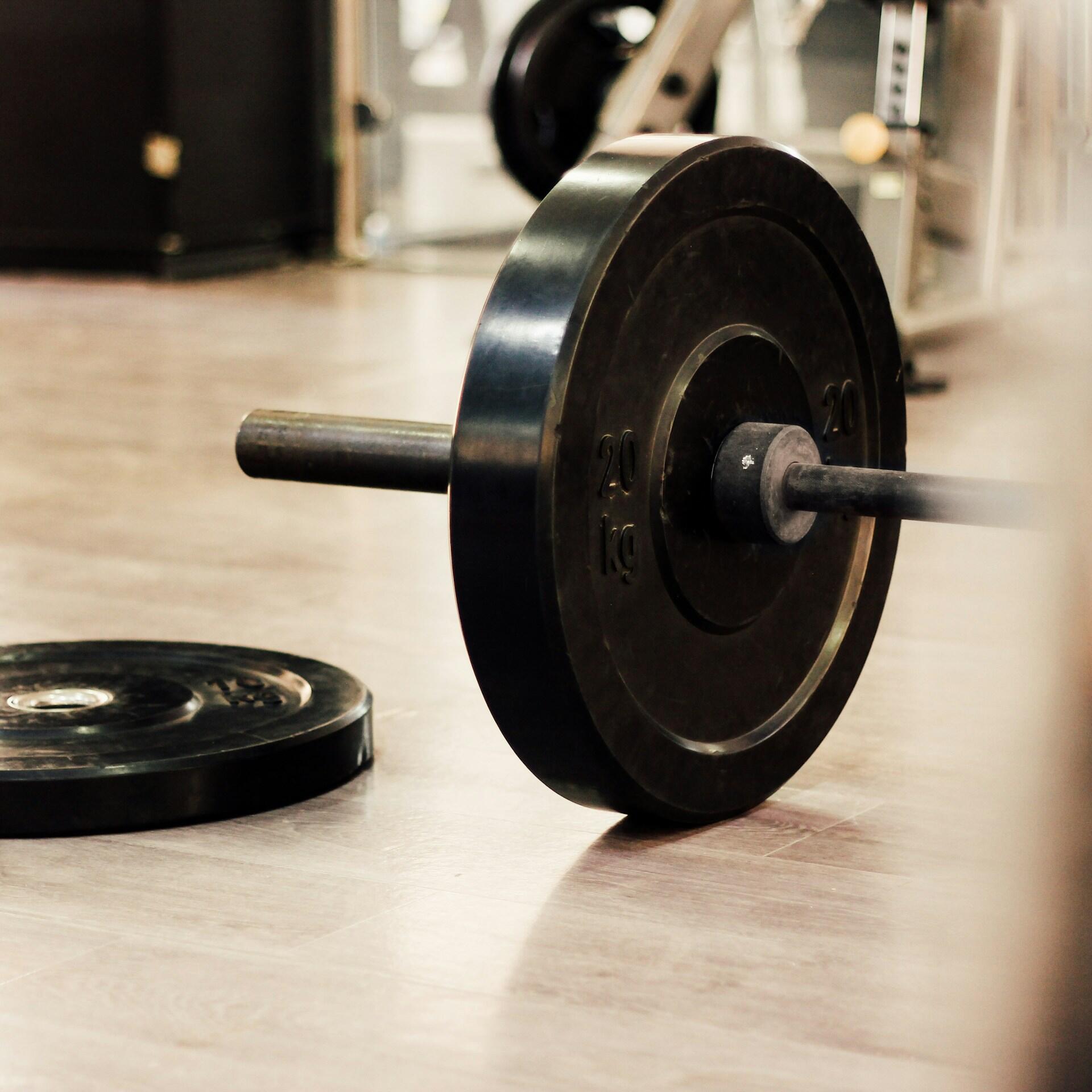 Primer plano de una barra con discos de 20 kg en el suelo de un gimnasio. La imagen transmite fuerza y concentración en un entorno deportivo.