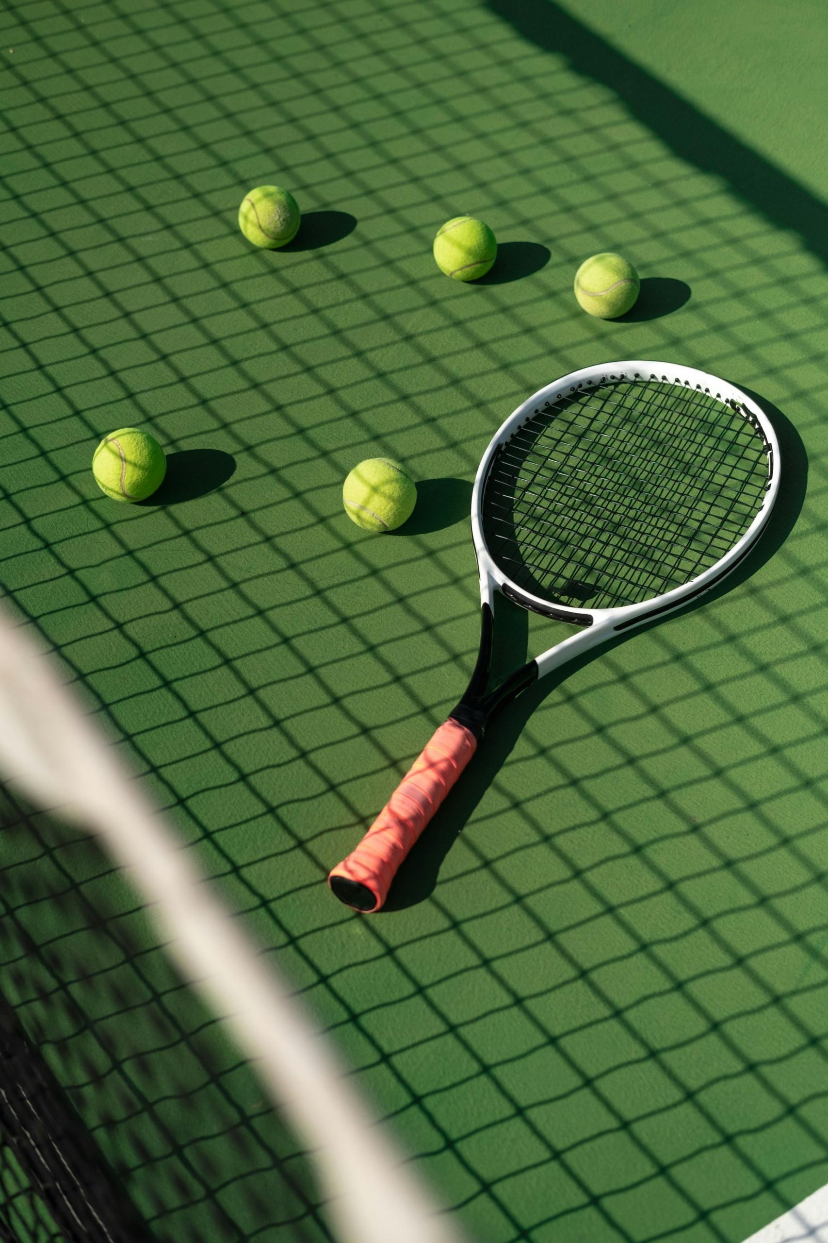 Raqueta de tenis y pelotas amarillas en una pista verde con sombras.