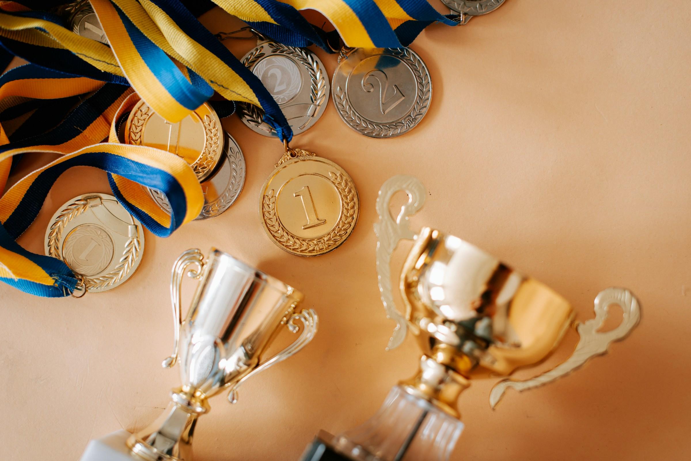 Medallas de oro, plata y bronce con cintas y un trofeo dorado sobre fondo beige.