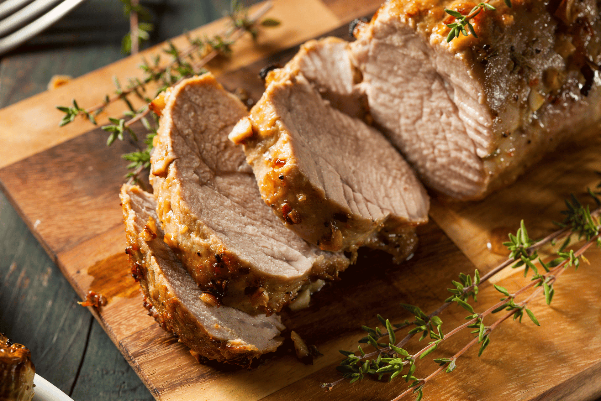 Un asado de cerdo en rodajas sobre una tabla de cortar, decorado con hierbas frescas.