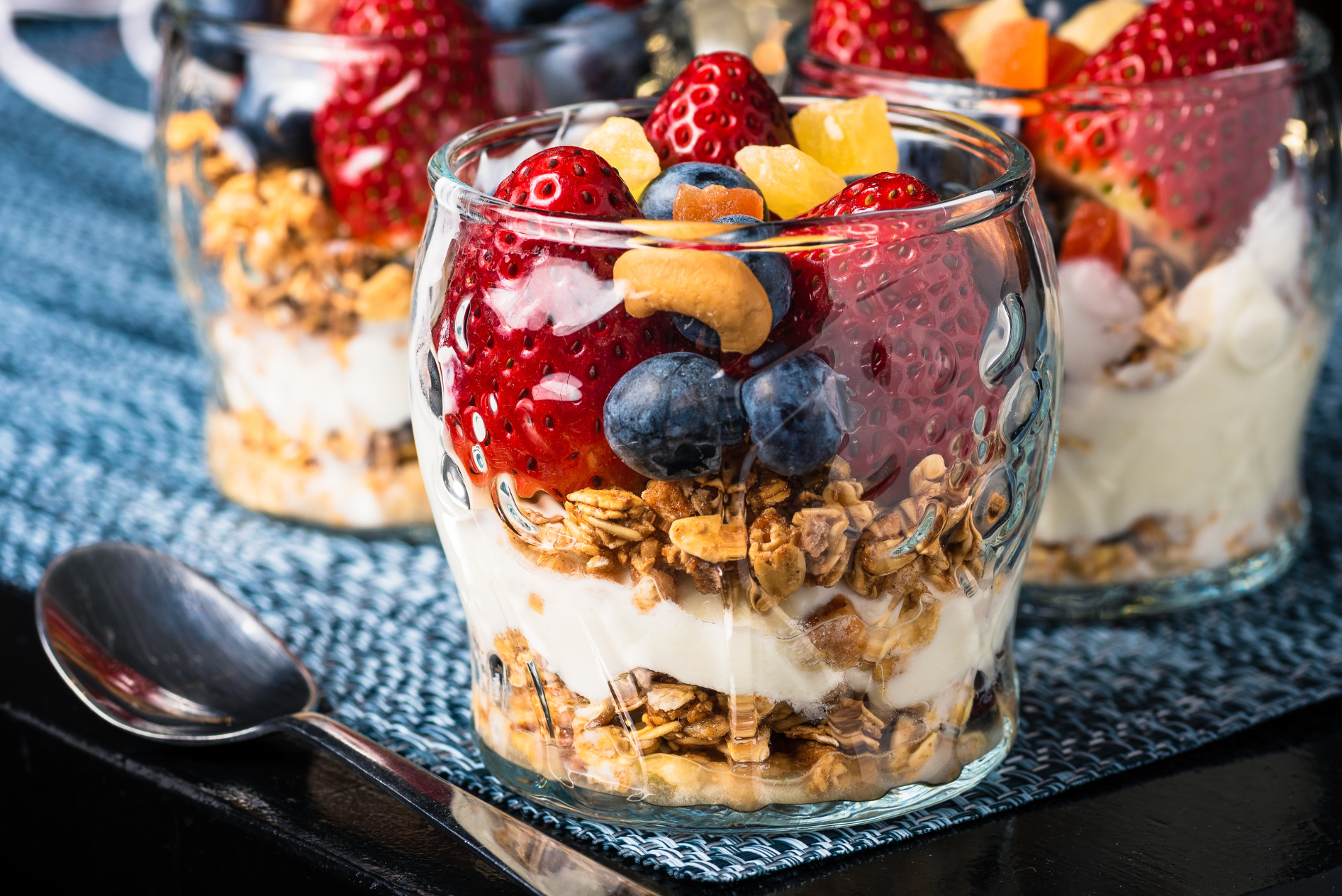 Un primer plano de un vaso de yogur con frutas frescas y granola crujiente.