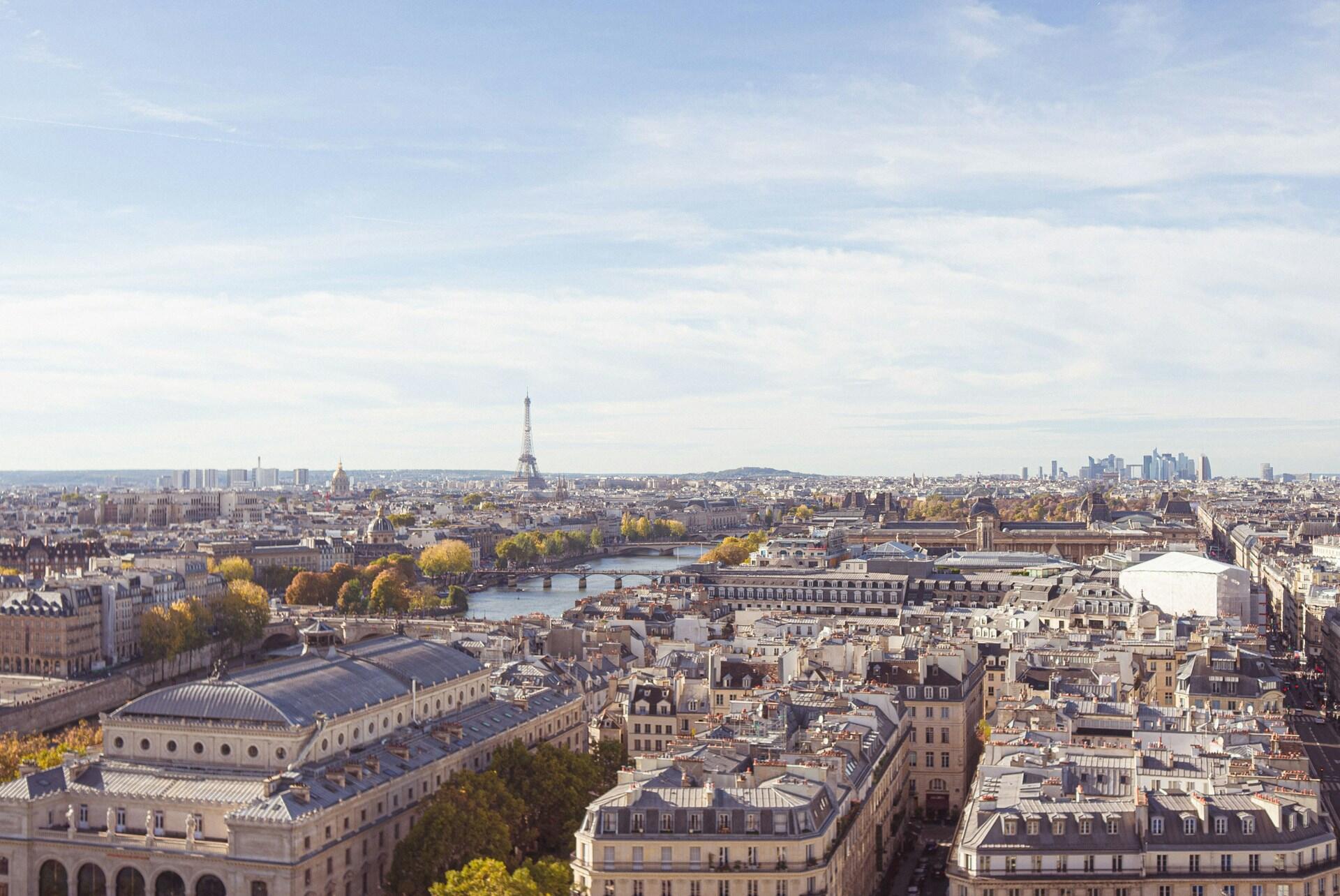 Vista aérea de París con la Torre Eiffel al fondo, el río Sena atravesando la ciudad y la arquitectura clásica de Haussmann bajo un cielo despejado.