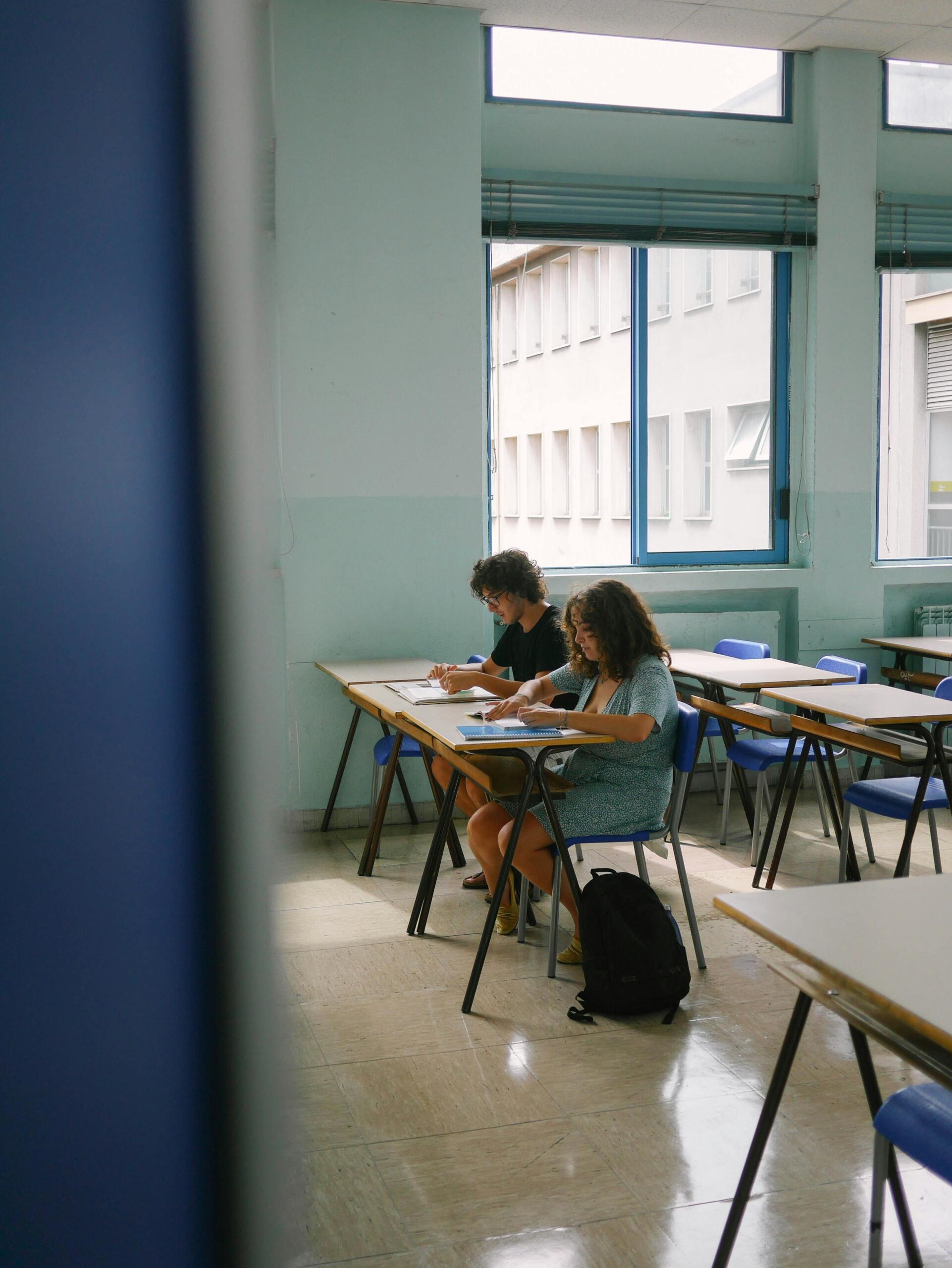 Dos estudiantes sentados en los pupitres de una clase trabajando en sus tareas.