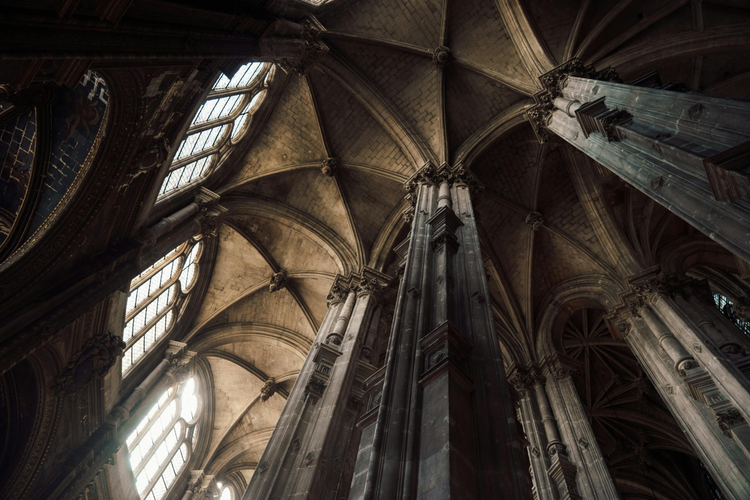 Interior de una catedral gótica con imponentes columnas de piedra, arcos intrincados y vidrieras iluminadas. 