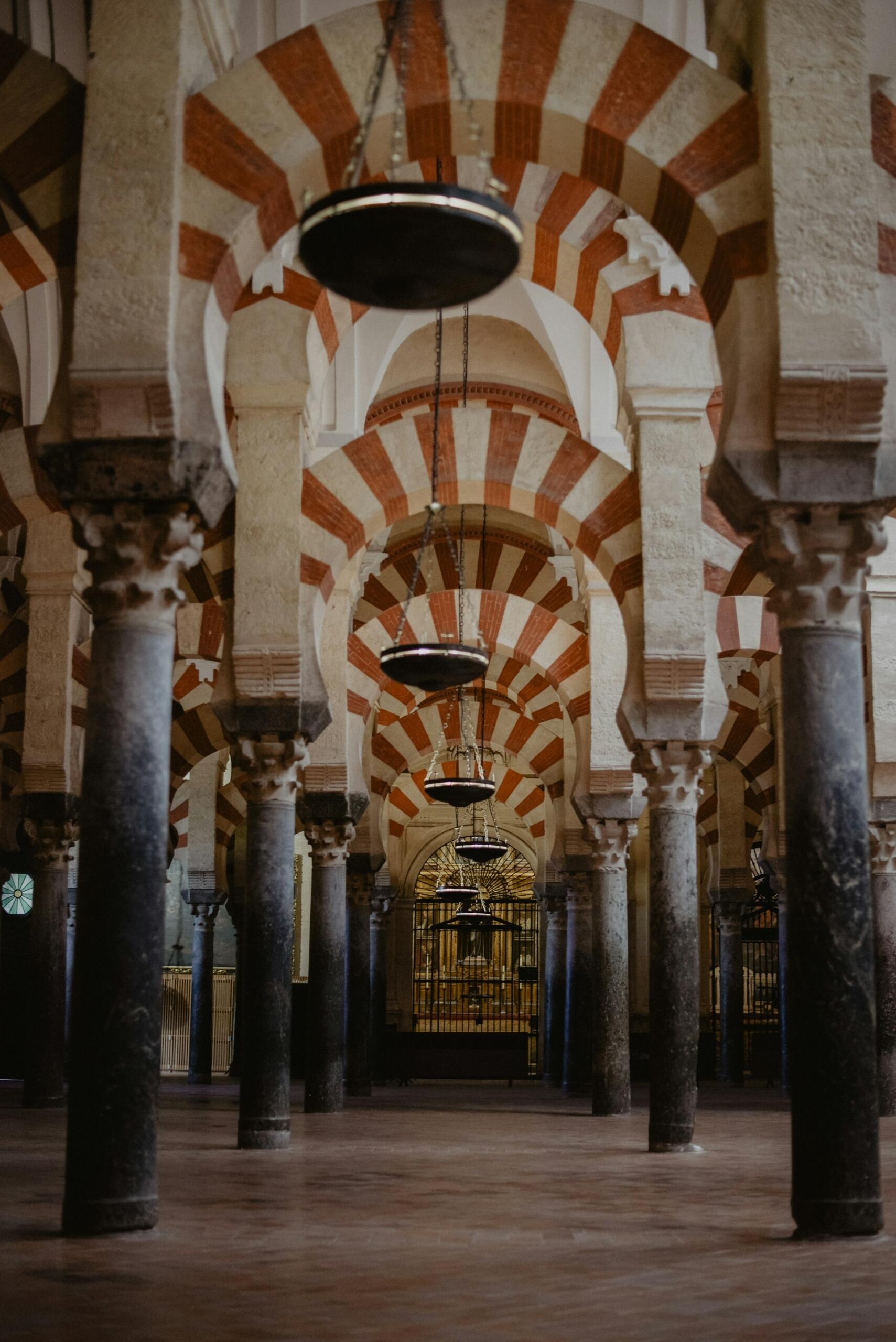 Interior de la Mezquita de Córdoba, con arcos de herradura rojos y blancos que se repiten, columnas de piedra, lámparas colgantes y un ambiente tranquilo e histórico.