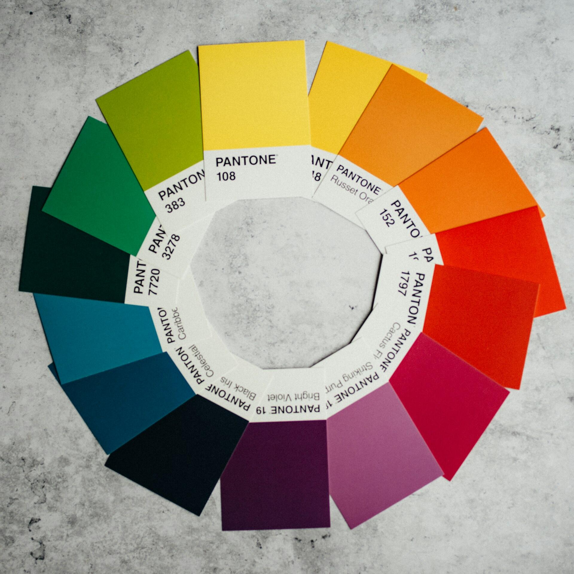 Una disposición circular de muestras de colores Pantone sobre un fondo de mármol, que muestra un vibrante degradado que va del verde y el amarillo al rojo y el rosa.