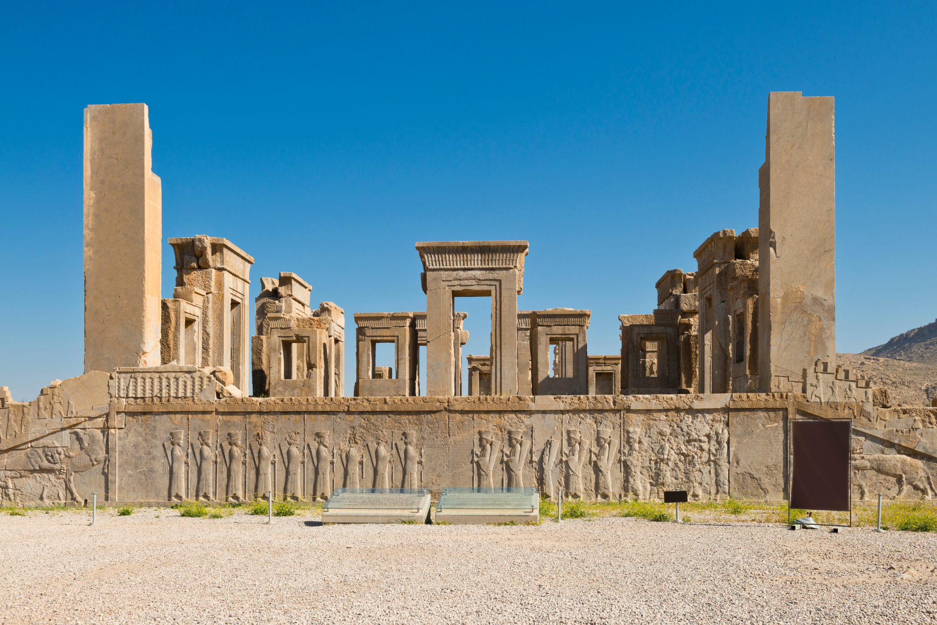 Antiguas ruinas de piedra con relieves tallados y altas columnas bajo un cielo azul despejado.