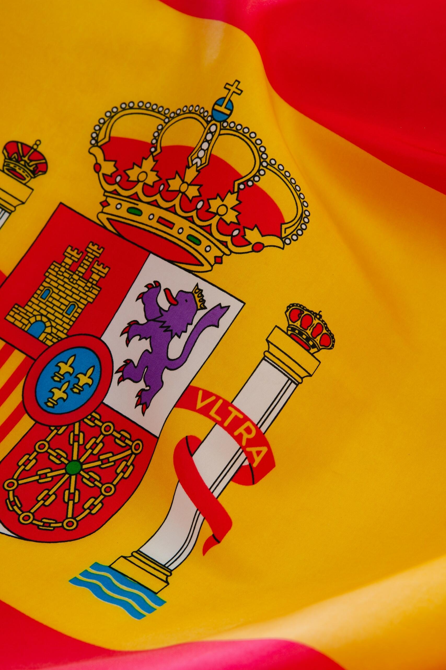 Primer plano de la bandera española, con sus vivos colores y el escudo nacional, que incluye una corona y un león morado.