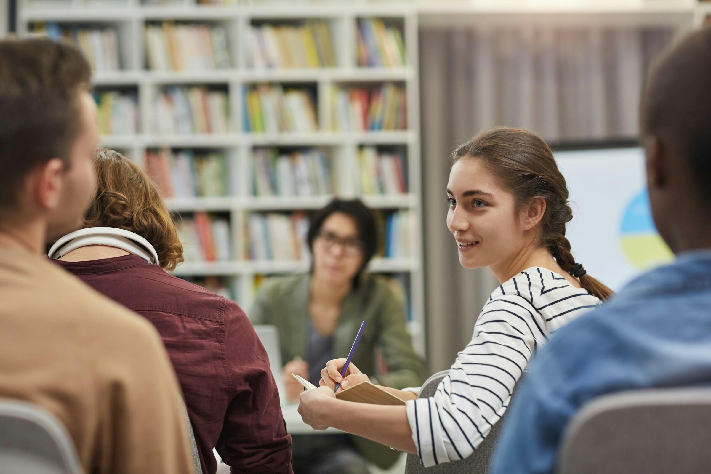 Un grupo de personas en un seminario, atentas a un ponente y a una presentación, rodeadas de estanterías.