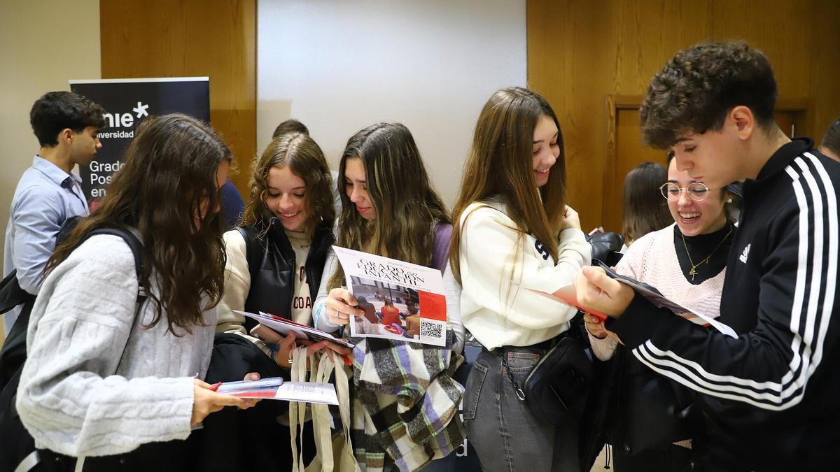 Un grupo de adolescentes sonrientes posan juntos en un interior, sosteniendo folletos. Parecen interesados y emocionados. Al fondo se ve una pancarta de la universidad.