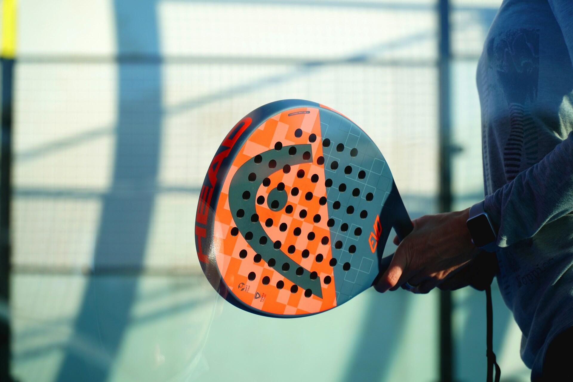 Persona sosteniendo una pala de pádel con un diseño azul y naranja.