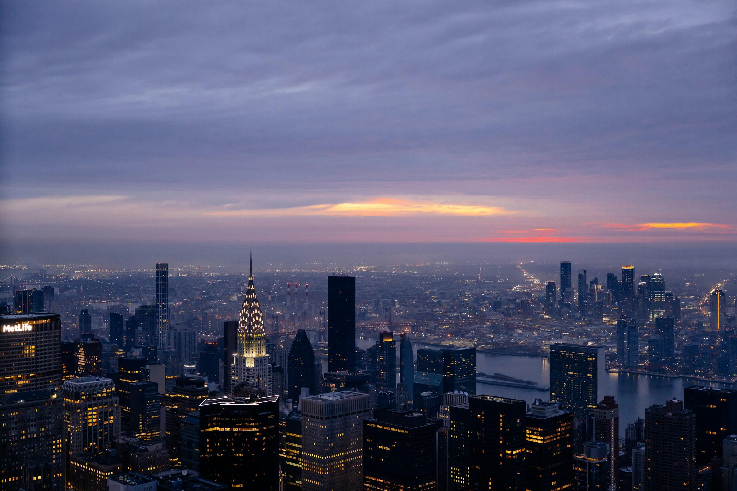Un horizonte crepuscular de Nueva York con el edificio Chrysler iluminado, luces lejanas y un horizonte colorido.