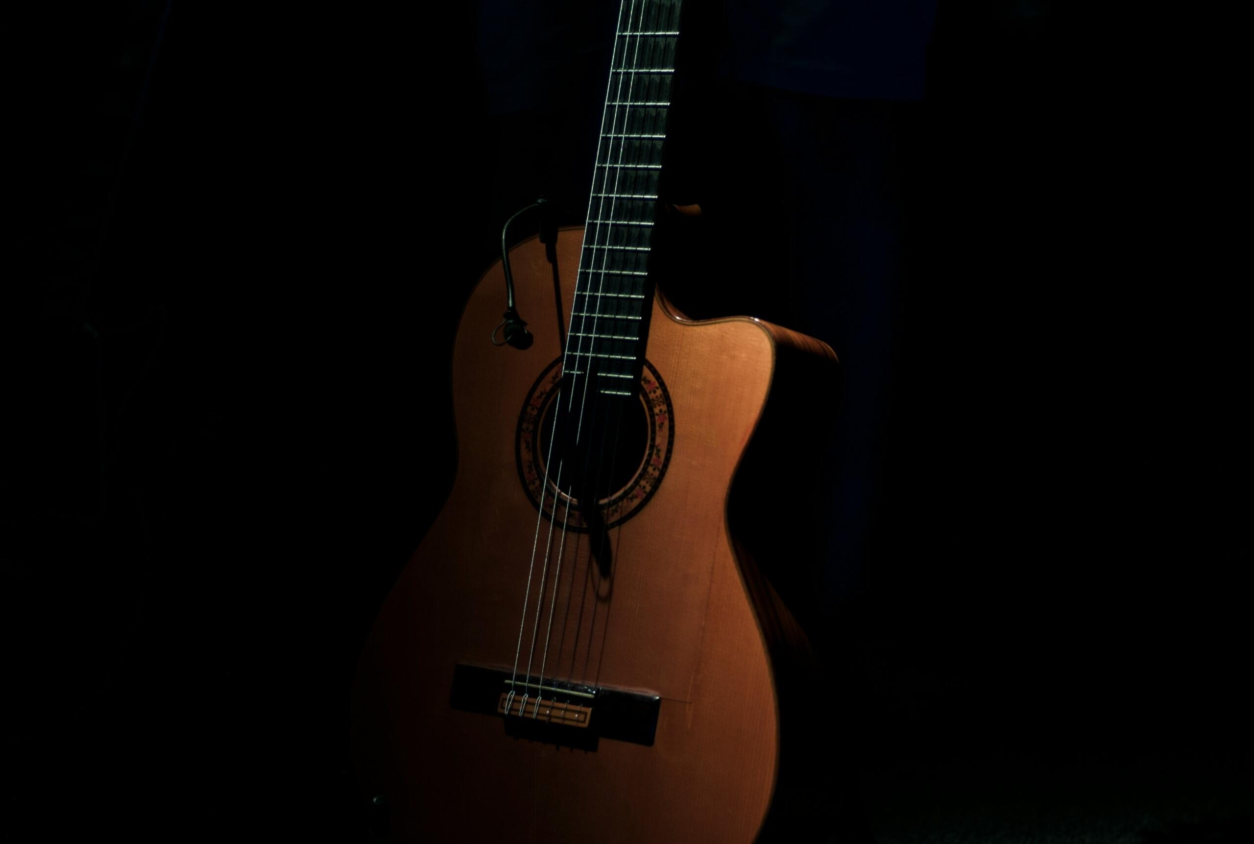 Primer plano de una guitarra acústica con poca luz, en el que destaca su cuerpo de madera y el intrincado diseño de su boca.