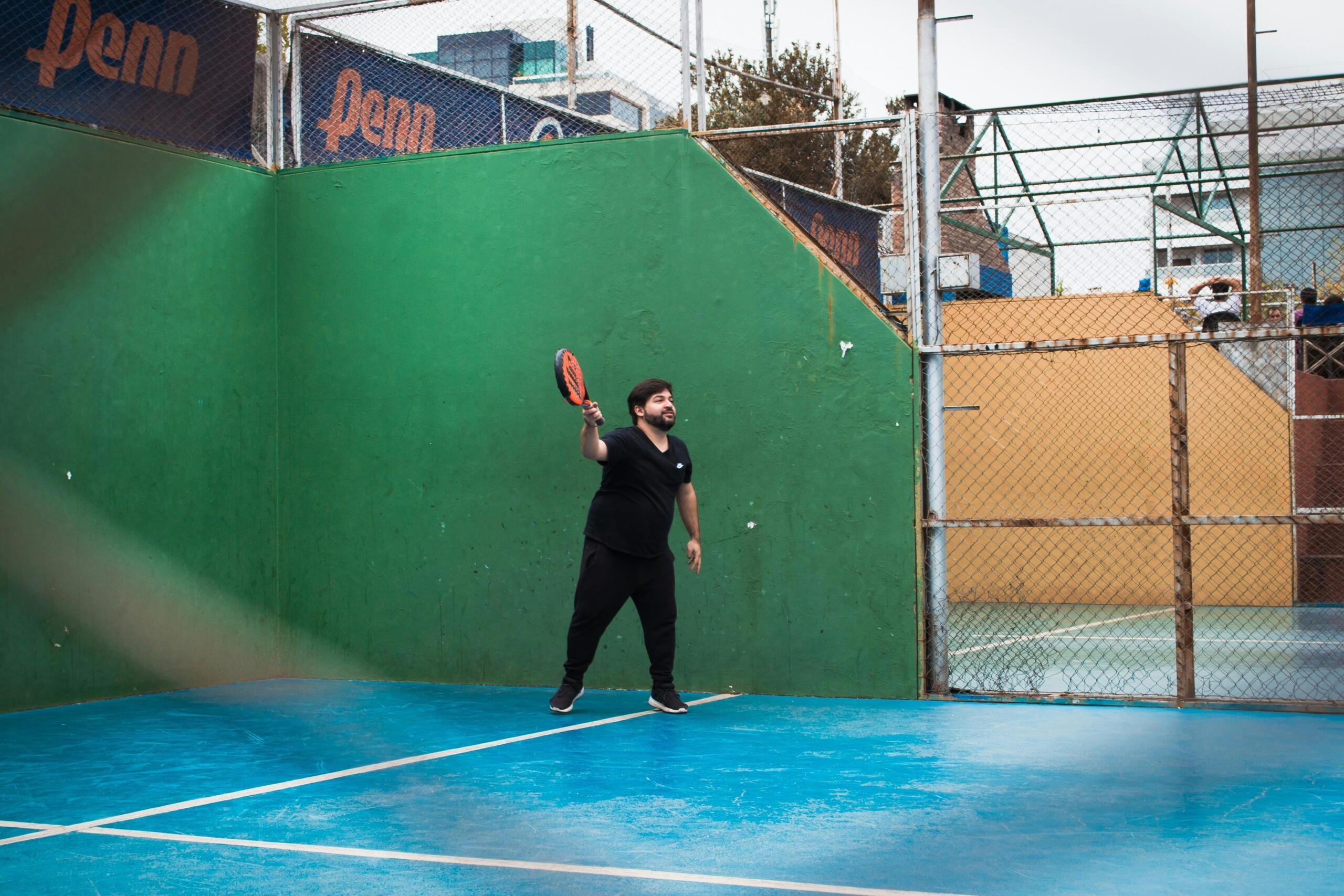 Hombre sosteniendo una pala de pádel en una cancha, listo para jugar.
