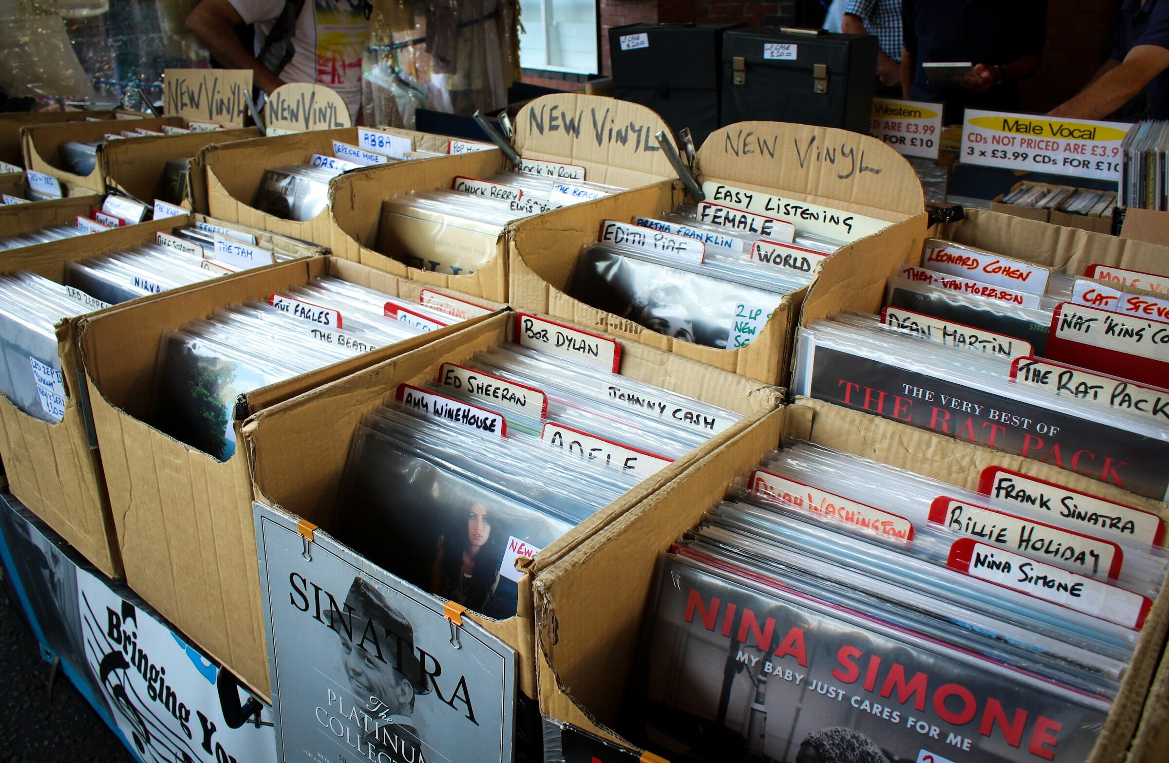 Una vibrante exposición de discos de vinilo organizados en cajas de cartón, con artistas como Nina Simone, Frank Sinatra y Ed Sheeran.